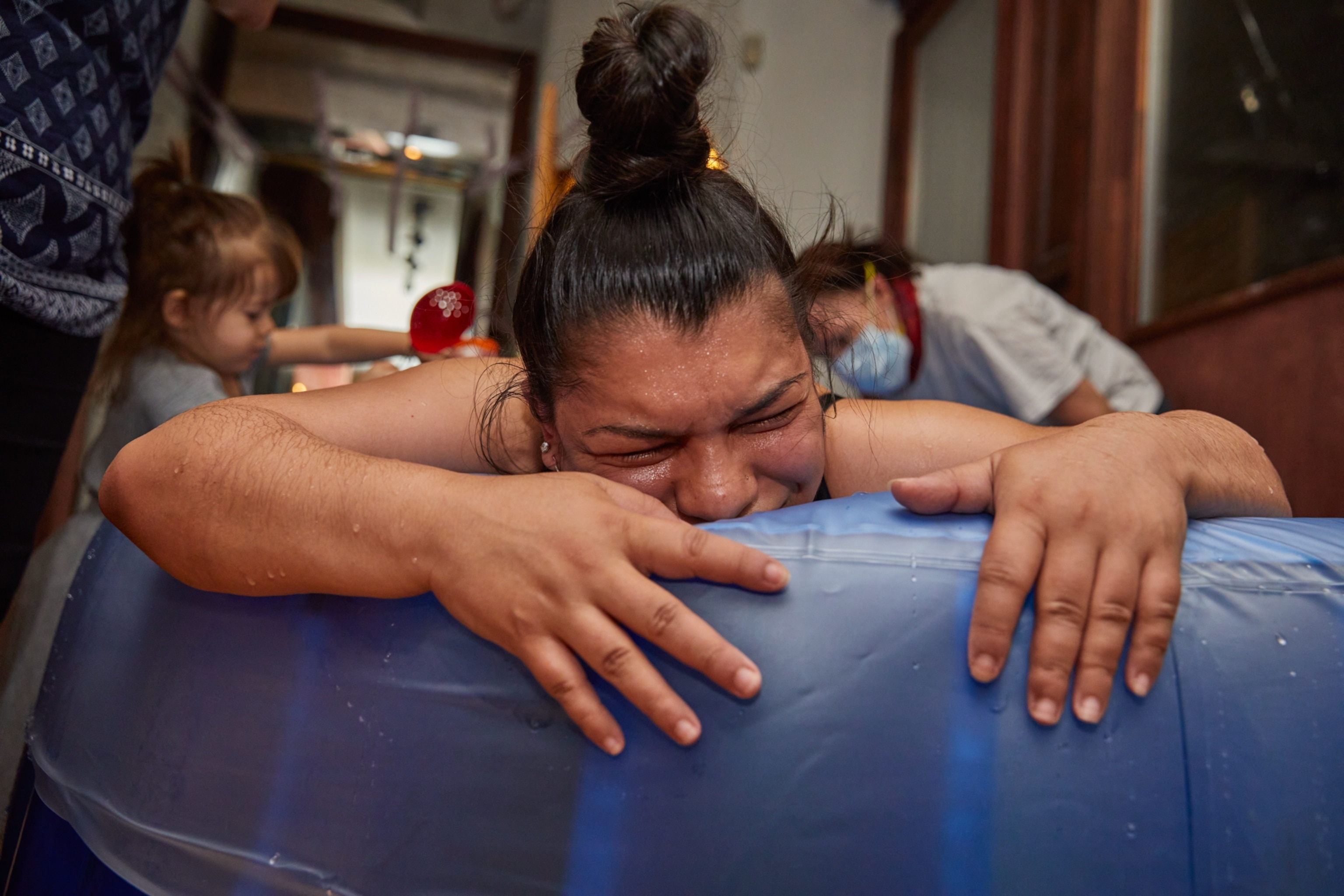 A woman's face scrunched in pain as she hugs the side of a baby pool while giving birth at home.