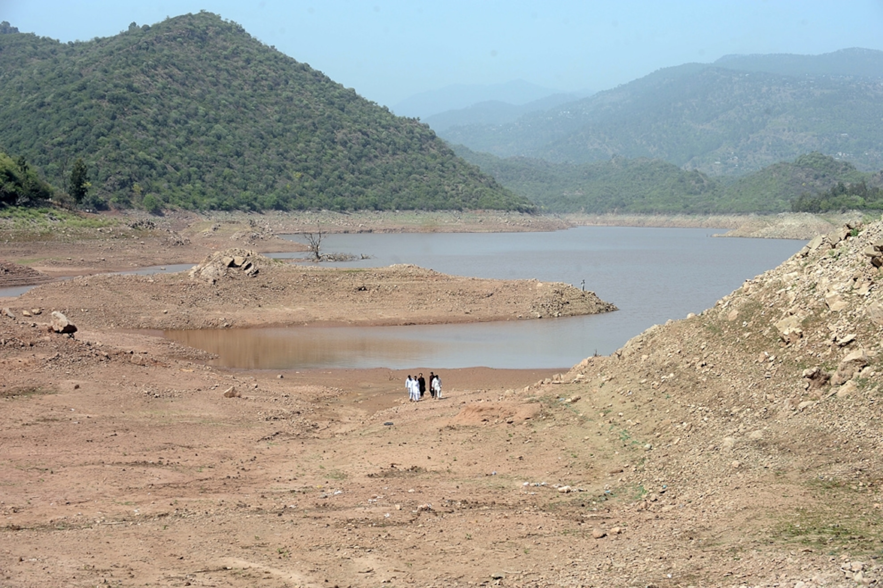 A few teenagers walk across a mostly dry lake bed from the water pool remaining in its center