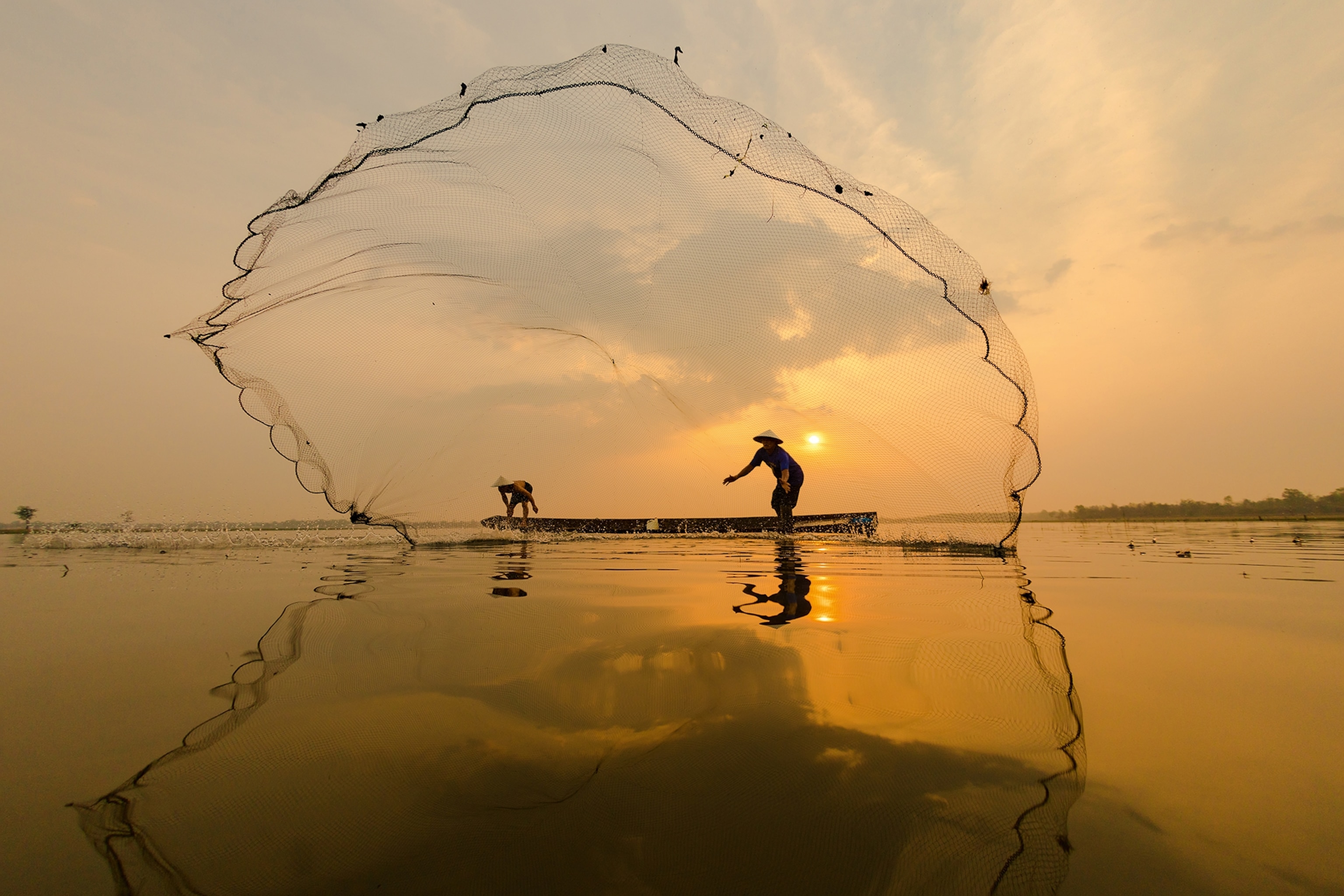 A dynamic shot of Laotian fishermen casting their nets across a river.