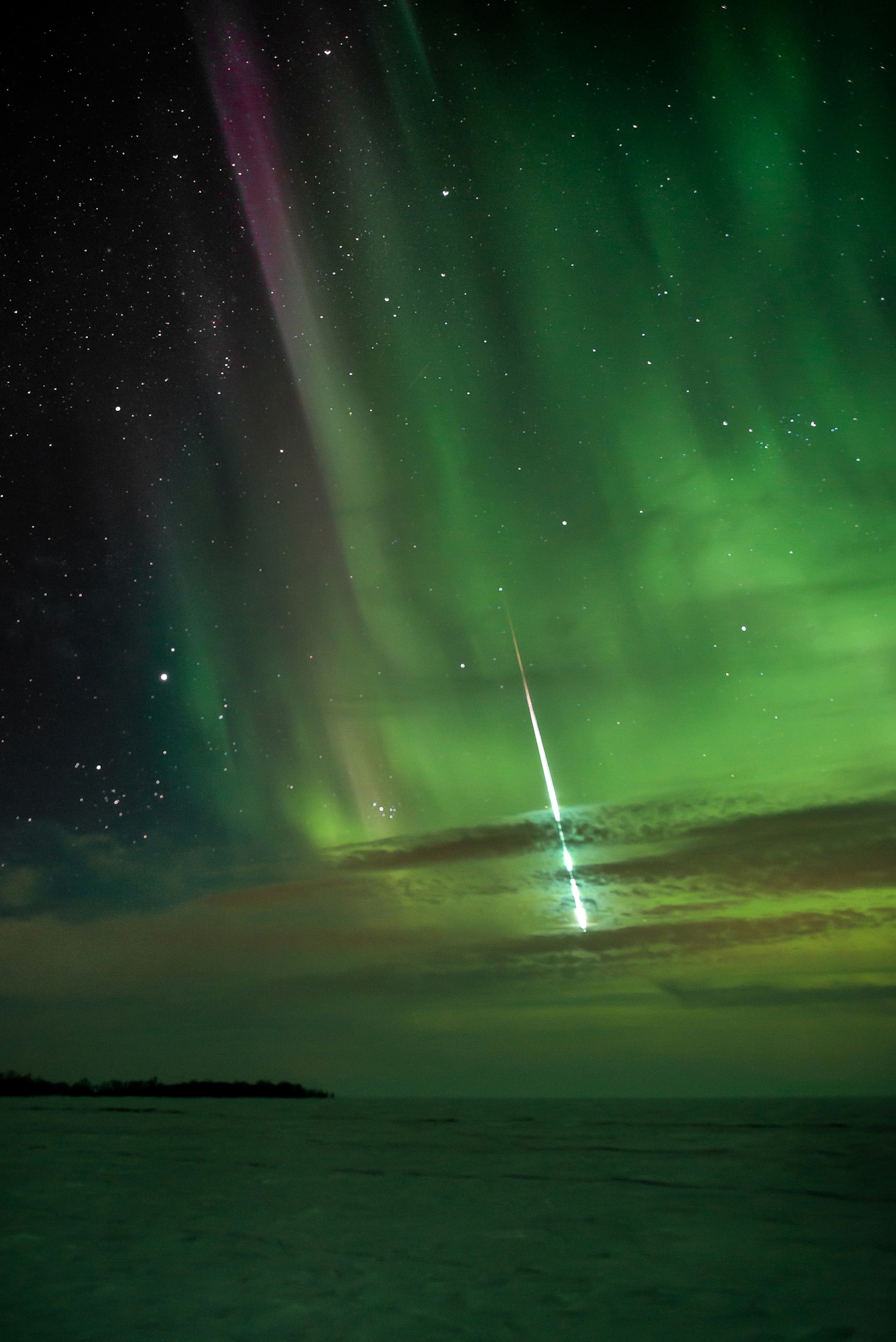 The World at Night - A picture of a meteor shooting through a green aurora.