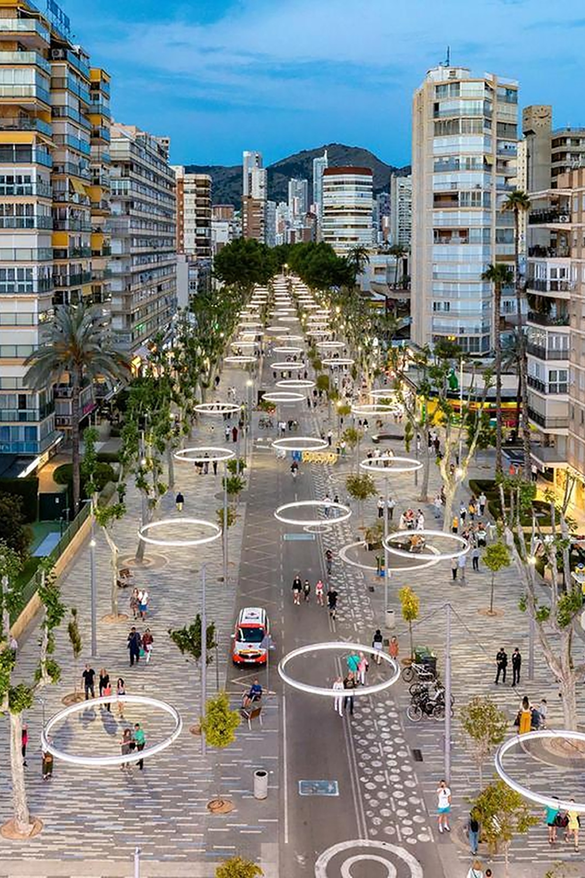Elevated view of a road surrounded by high-rise buildings, with circular illuminated lights hanging above the street from above