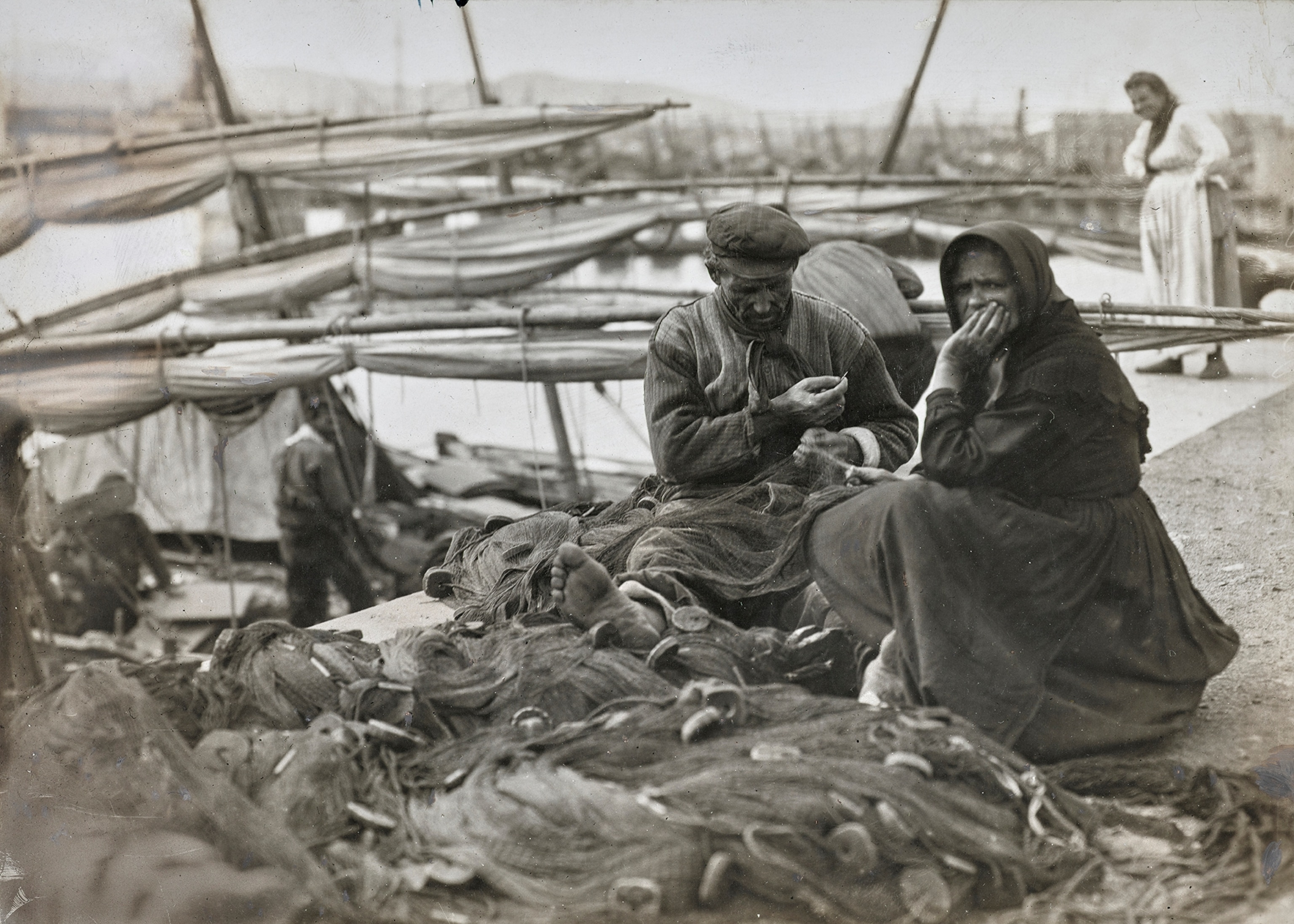A pair of fisherfolk work beside nets.