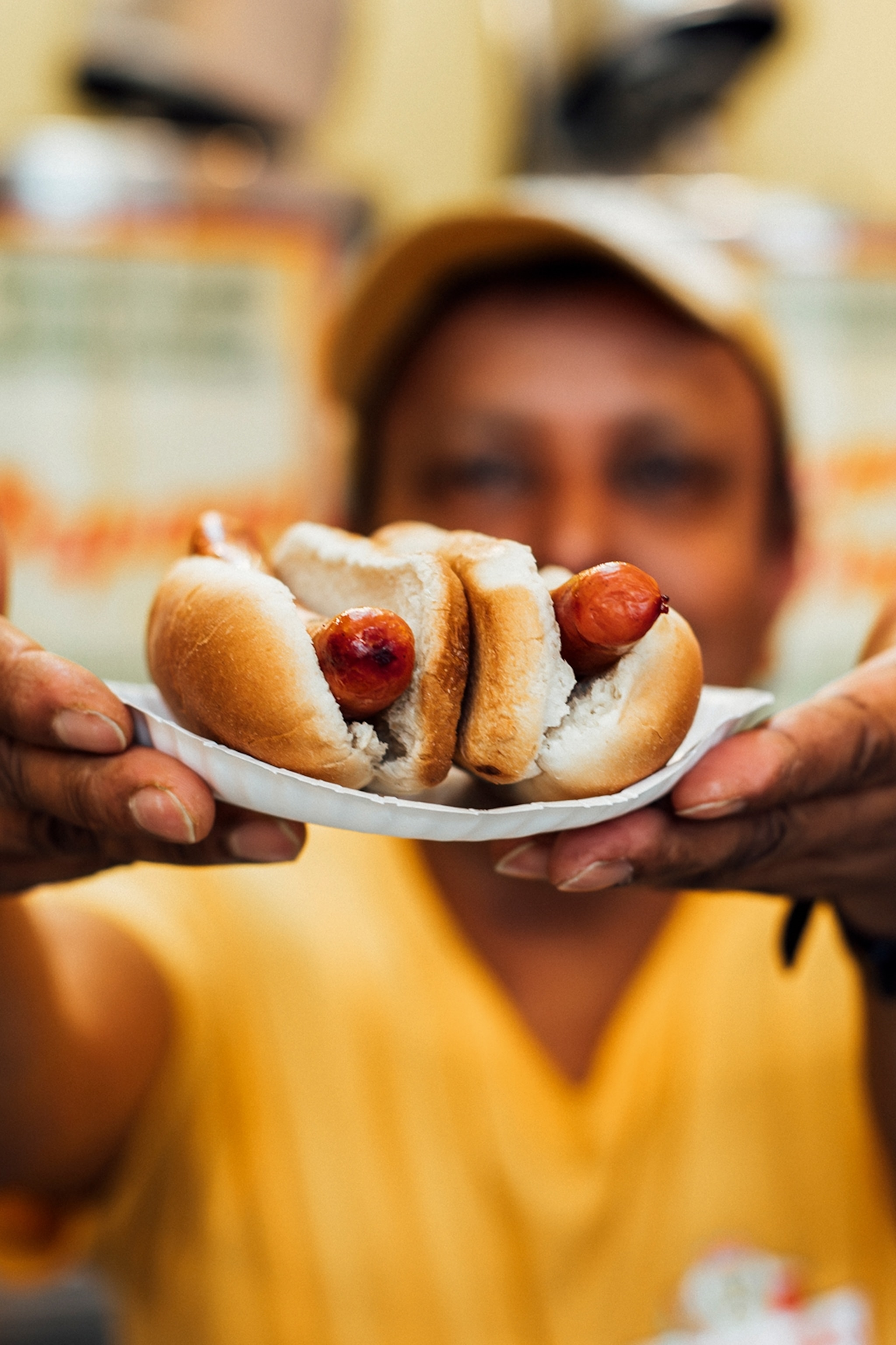 A hot dog vendor holding up a plate of the food item close to the camera.