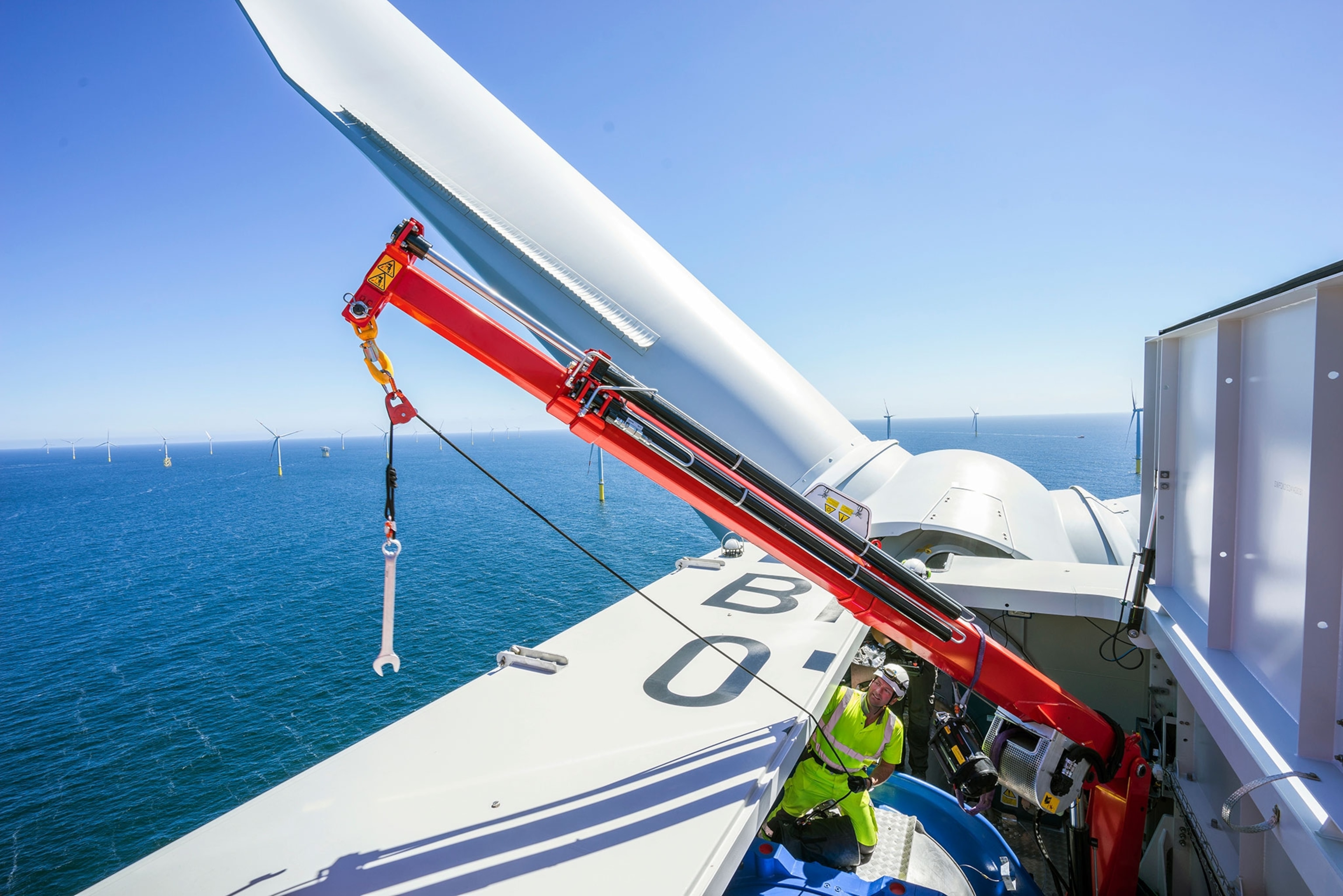 a Siemens worker on an offshore wind turbine using a crane to lower a wrench to workers below
