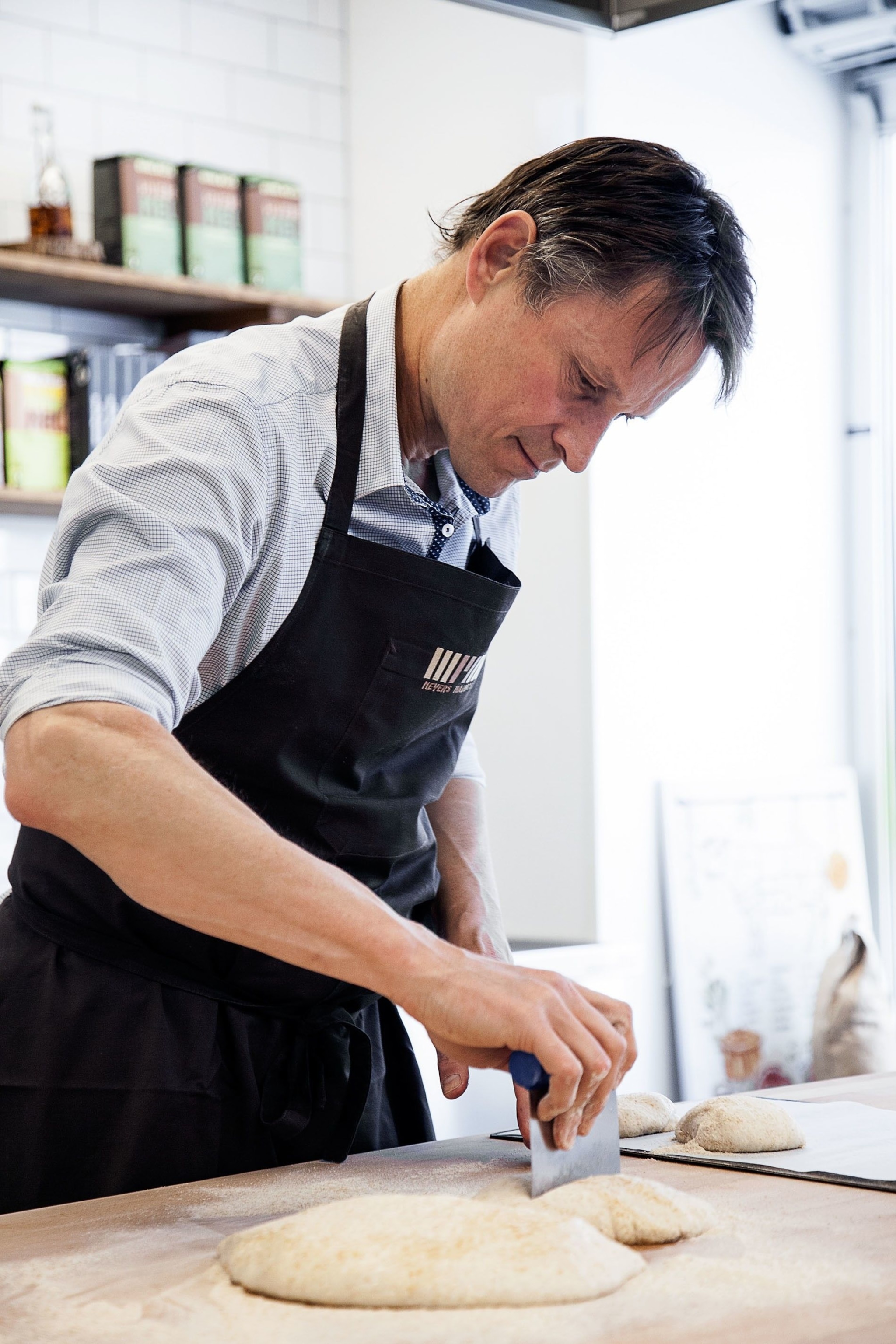 Here Claus Meyer, founder of the international chain Meyer's Bakery, slices dough to make kanelsnurrer cinnamon swirls. In many ways, he says, the Covid-19 crisis has wound up bringing him closer to his guests and customers. Alongside his colleagues and friends, Claus has started livestreaming cooking classes and talks through social media.