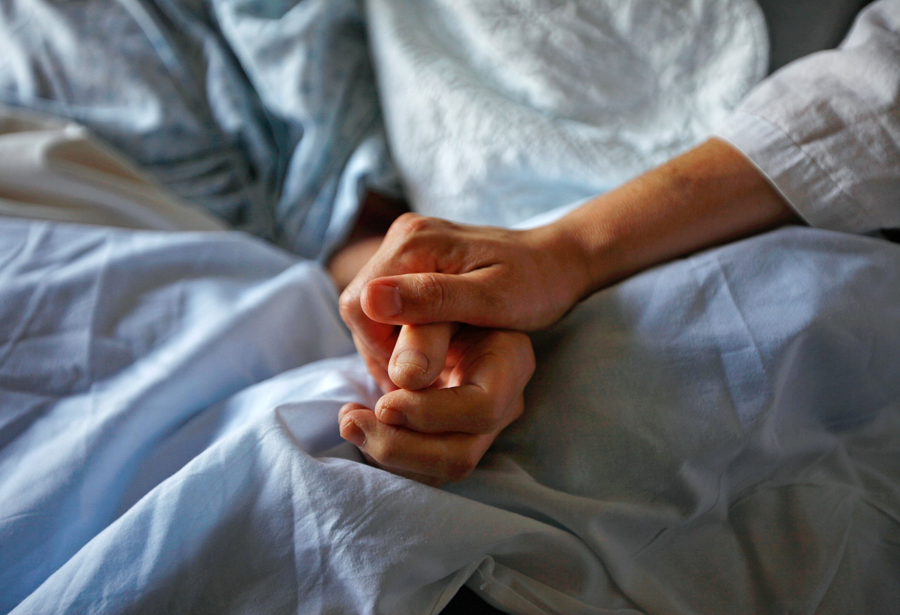 A woman holds the hand of her mother who has cancer.