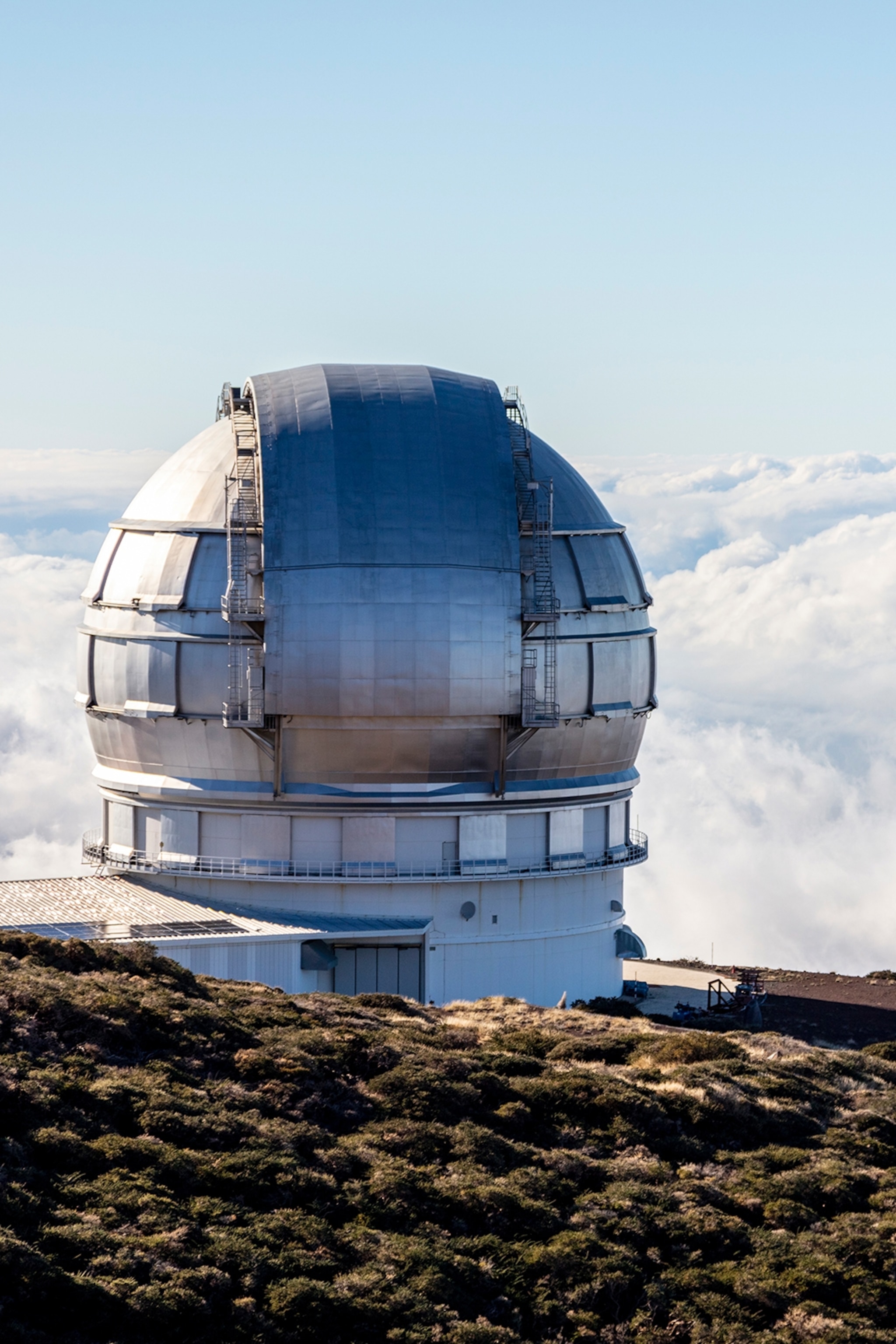 A globe-like observatory at the top of a hill overlooking clouds.
