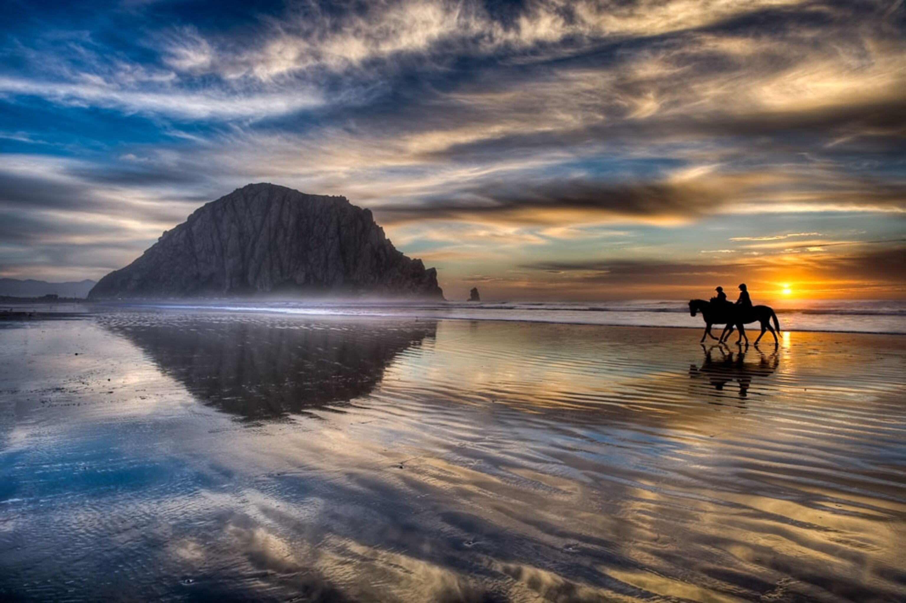Two equestrians trotting down the beach at Morro Bay