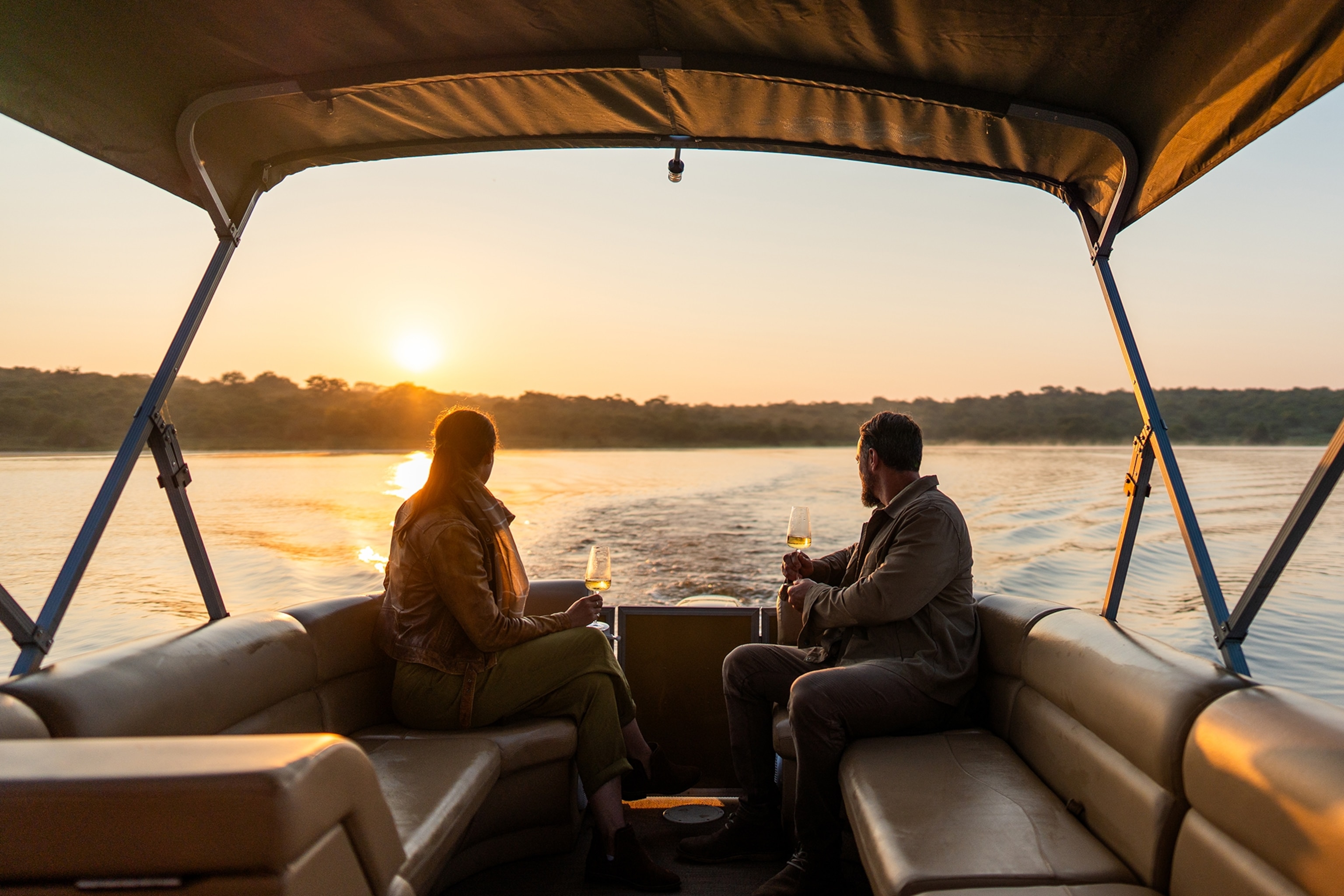 A couple drink wine on a sunset boat cruise in Rwanda's Akagera National Park.