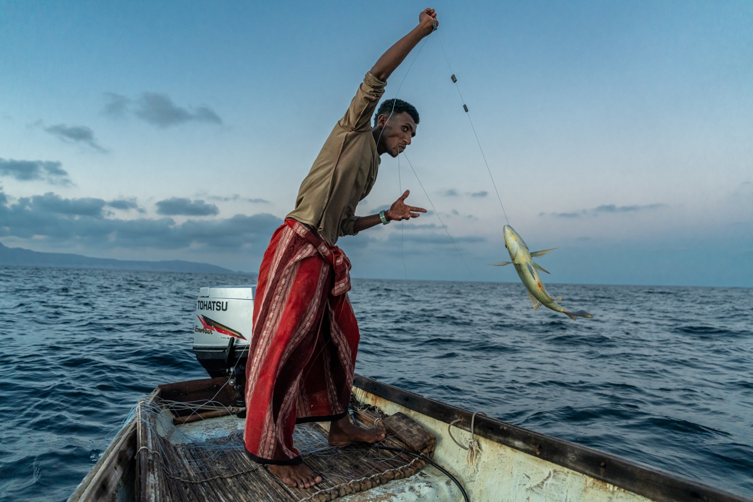 A fisherman pulls up his catch off the side of a small dhow.