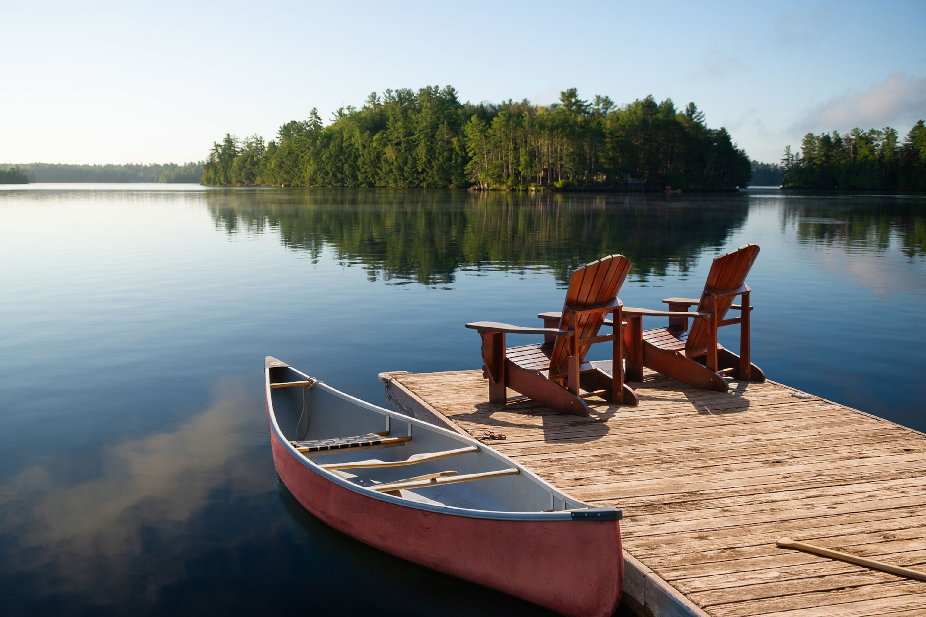 Adirondack chairs on a Muskoka dock with a canoe and lake view.