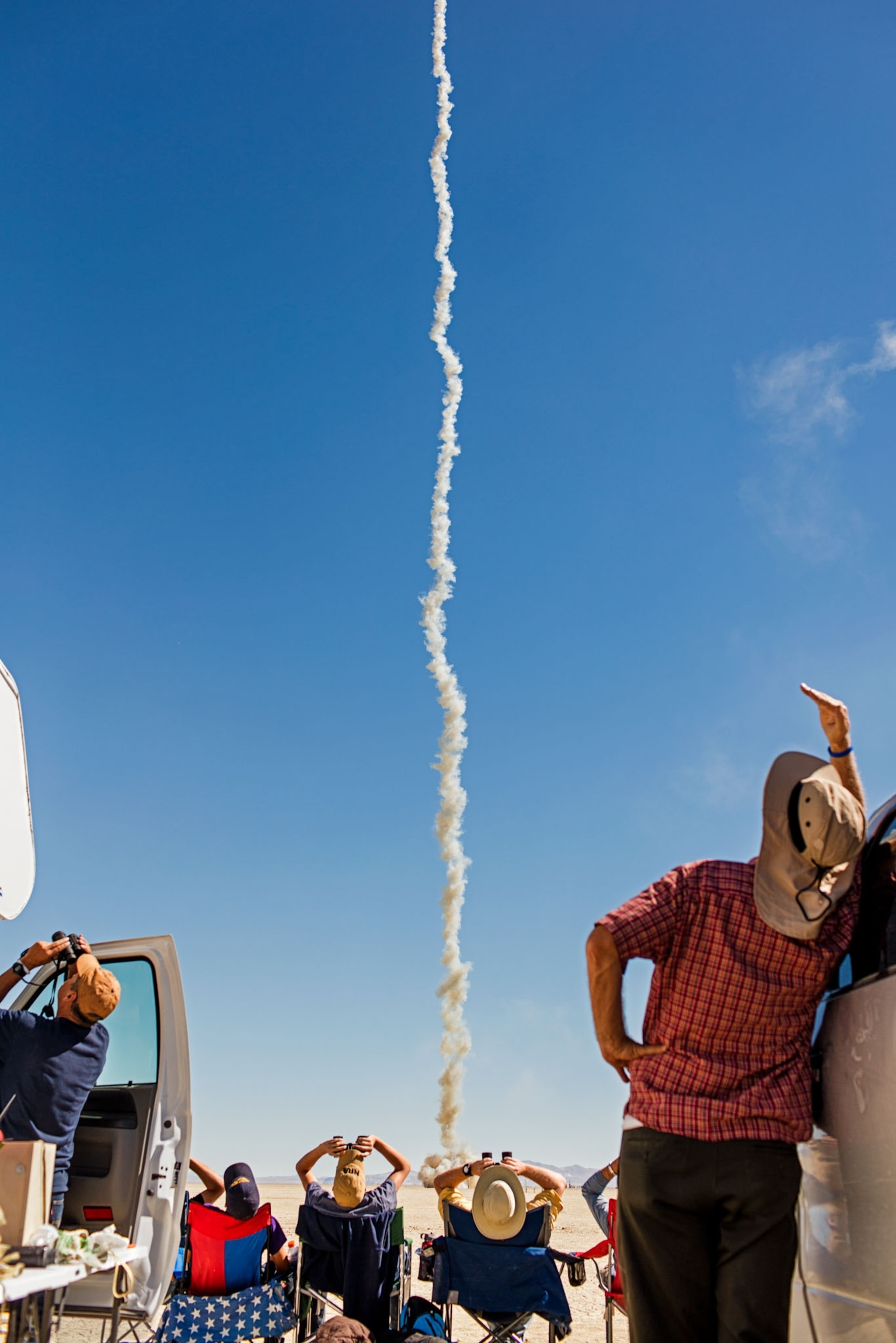 participants from behind looking up at a white rocket trail in a blue sky