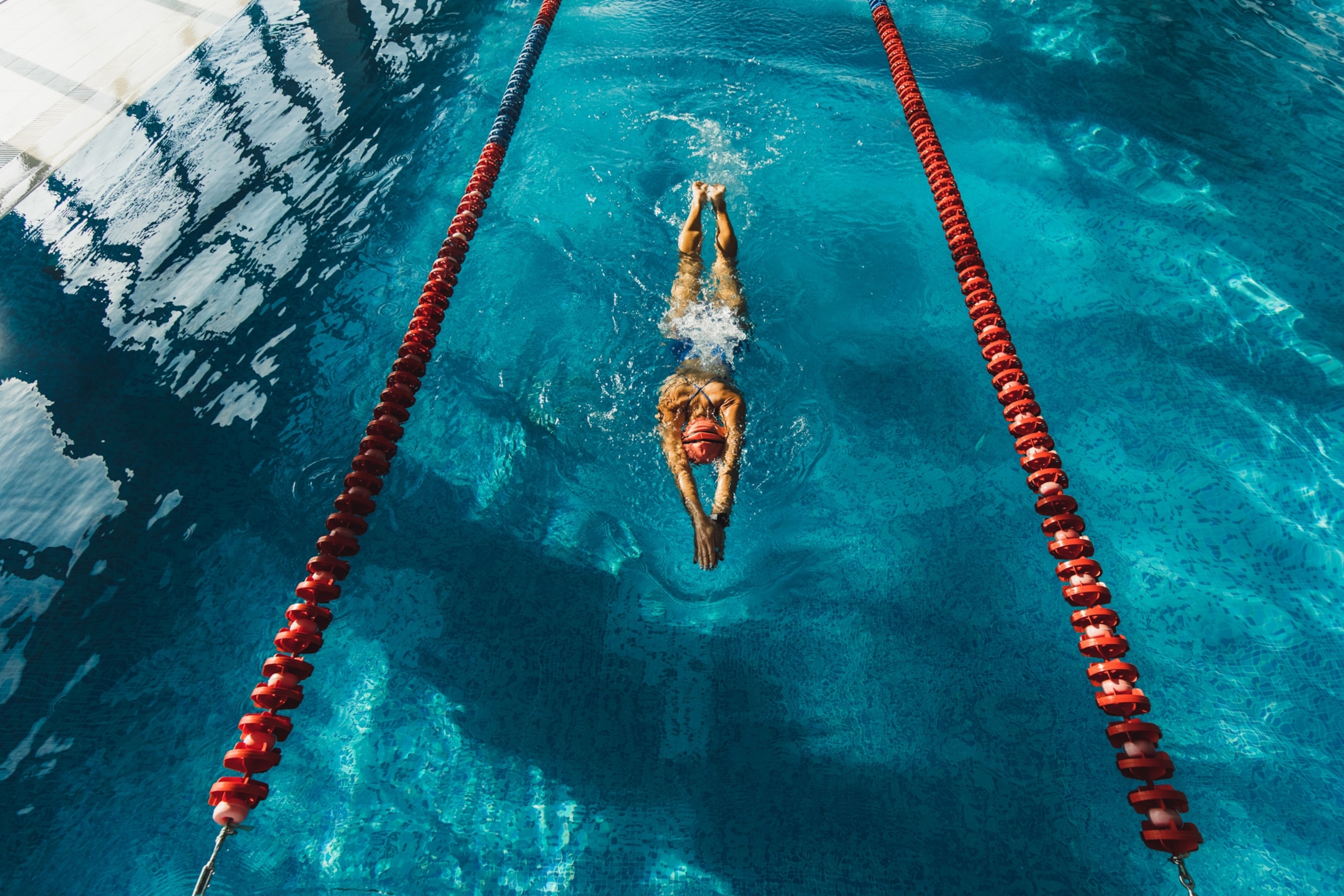 Aerial view of a swimmer doing laps in a clear blue pool, flanked by red lane dividers.
