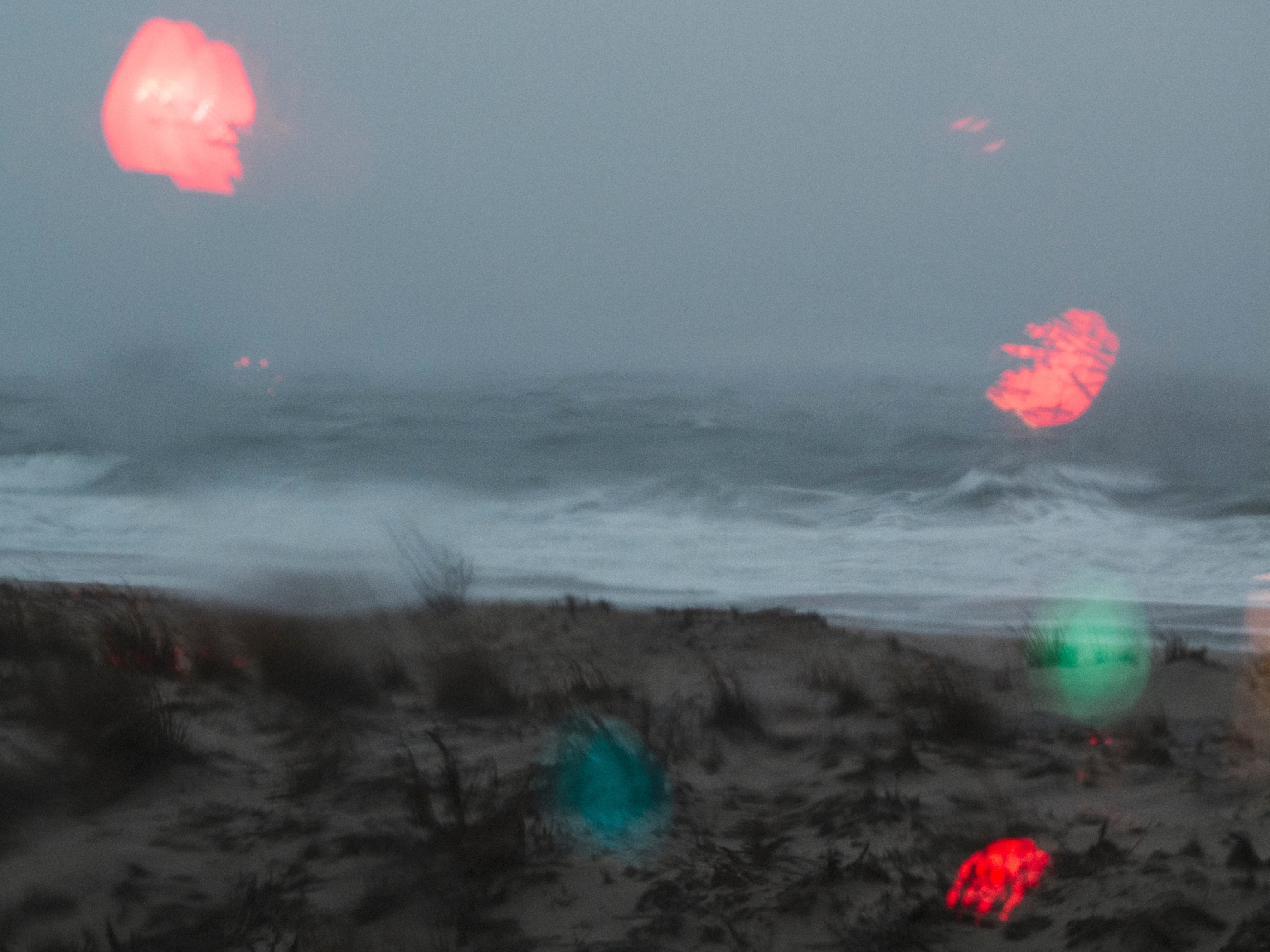 the ocean during a storm, seen through a window reflecting the bulbs of Christmas lights