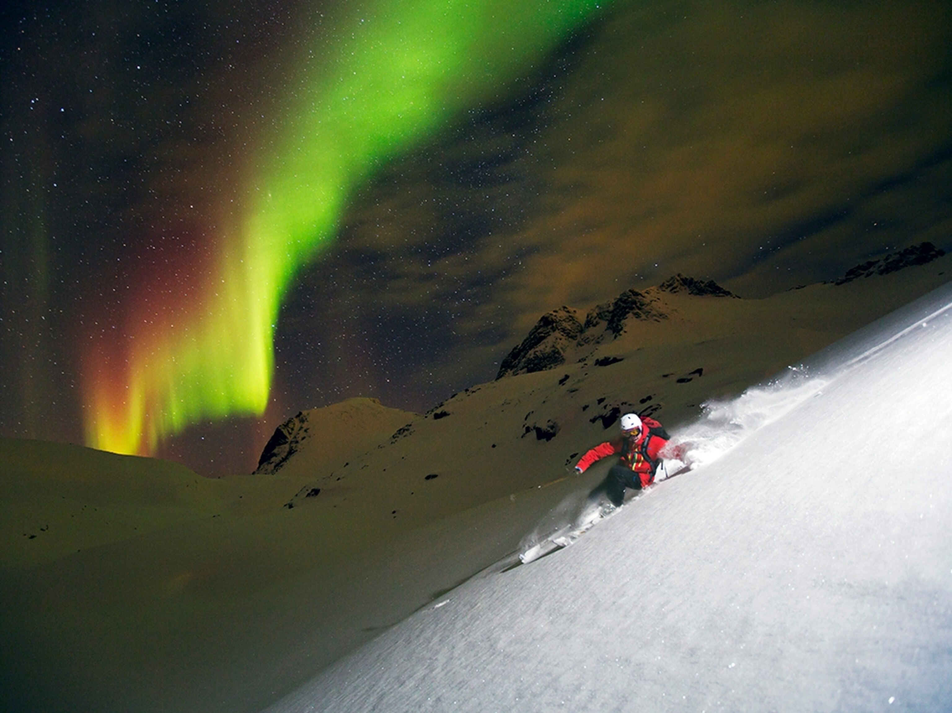 a man skiing down a mountain in Norway with the northern lights in the background