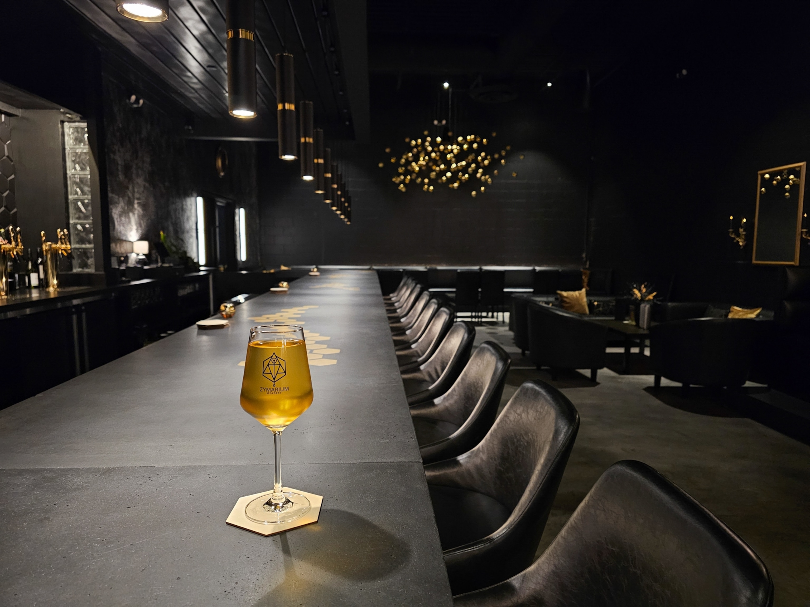A glass of golden colored mead, which contrasts against a dark black bar dotted with gold accents