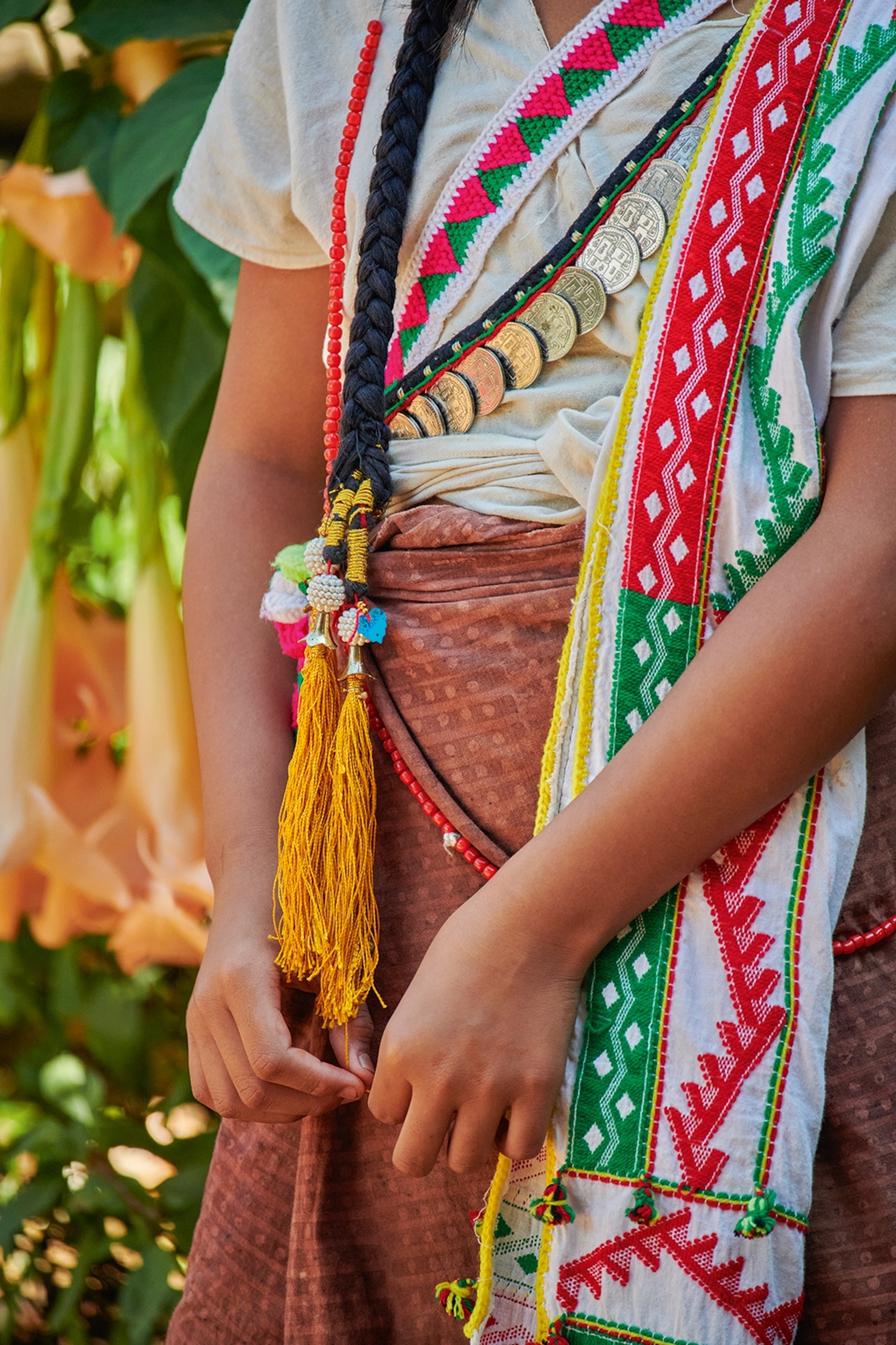 A close-up shot of a girl wearing wrap-around textiles with geometrical patters and coins along the seams.