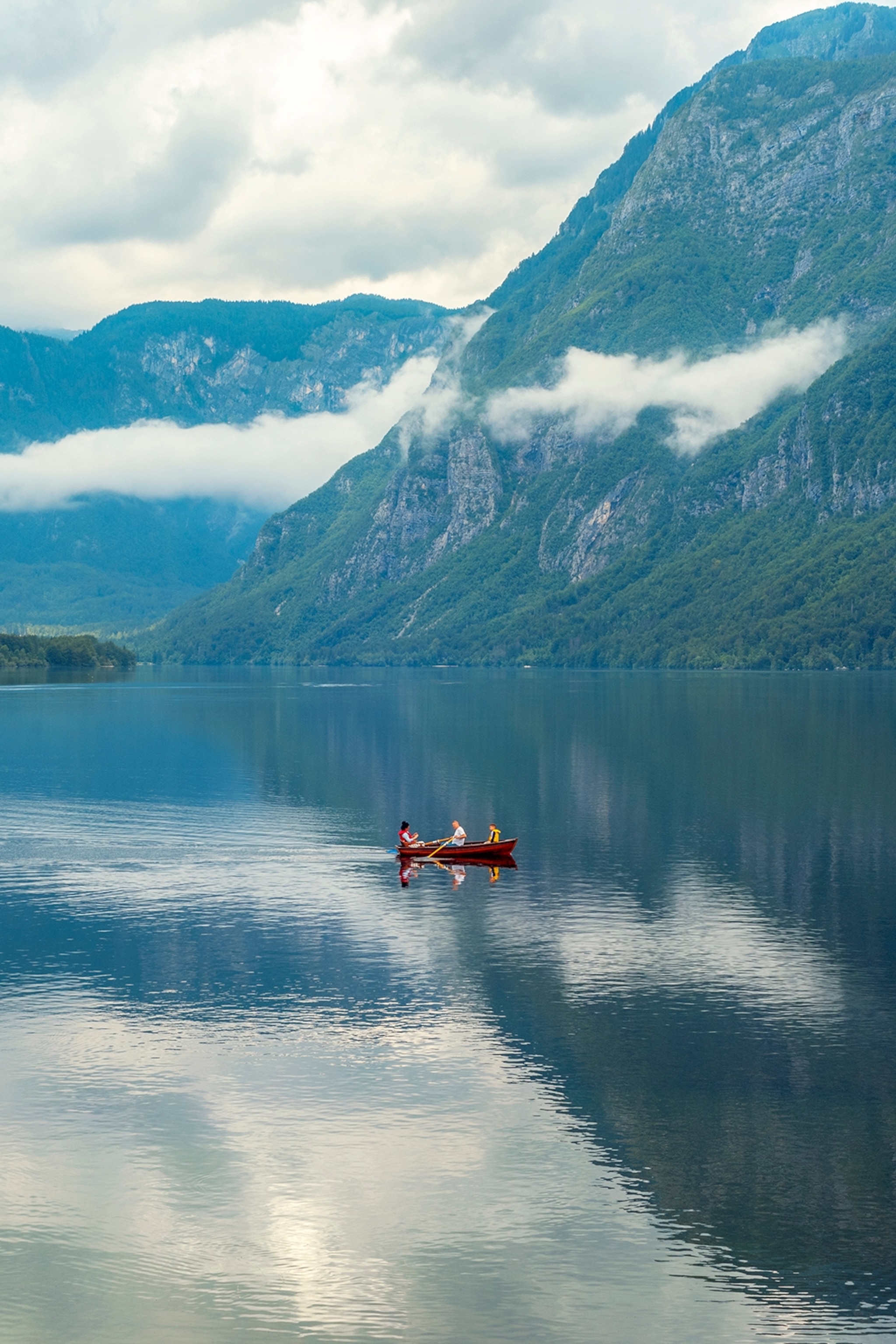 Two people in a canoe on a clear and still lake surrounded by mountains.