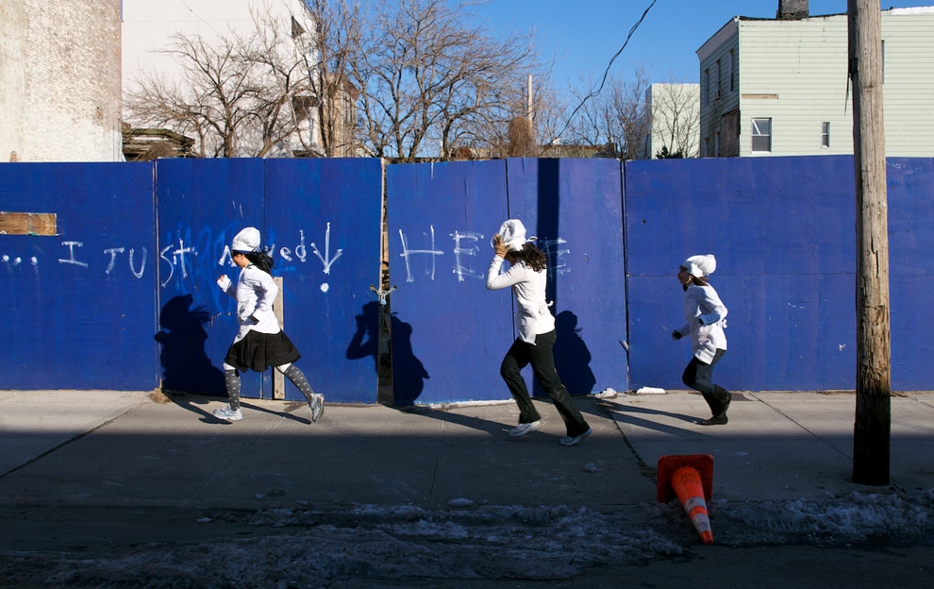 Three women dressed as bakers race alongside wall