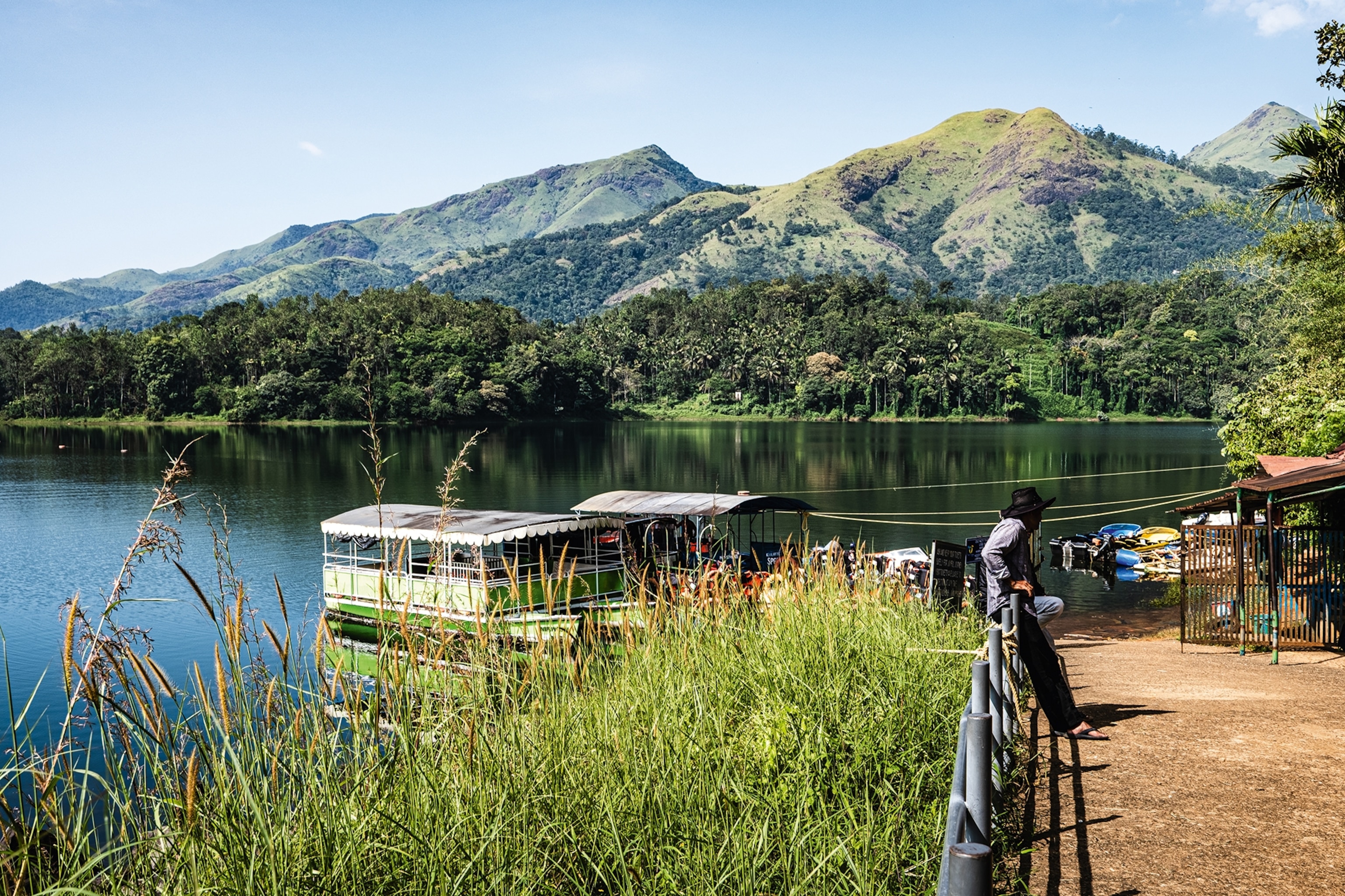 The bank of a lush river with a hill landscape in the background, with two river boats anchored on the shore.
