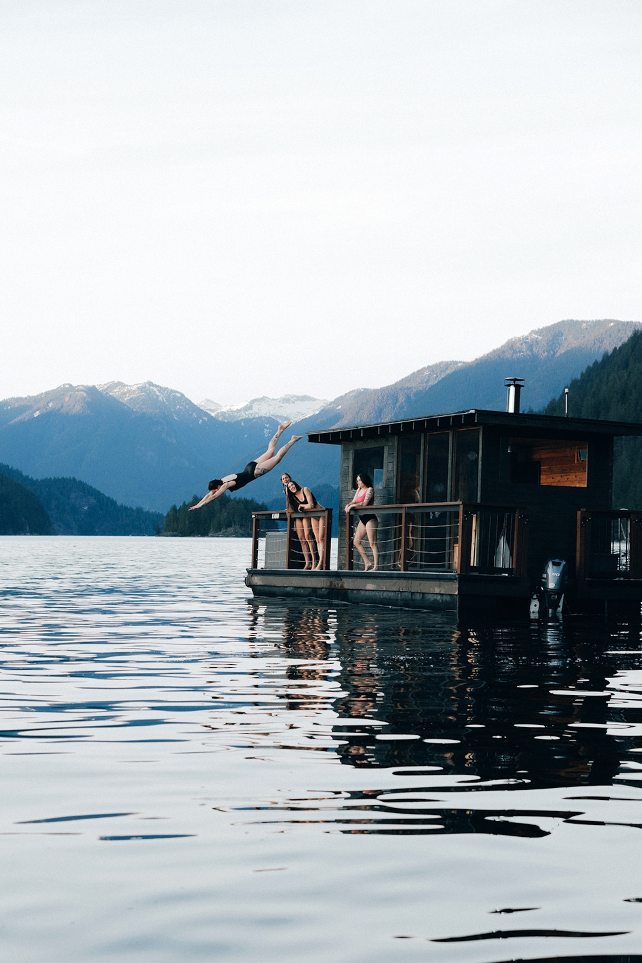 A floating sauna hut on a lake with mountains and forest in the background.