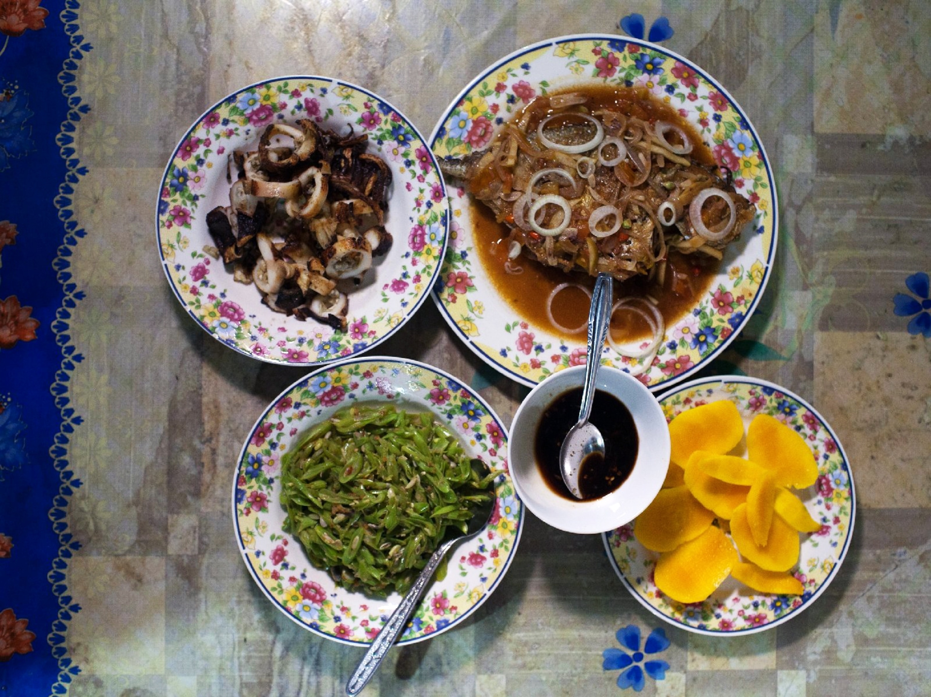 plates of greens, squid, fish and mango on a dinner table
