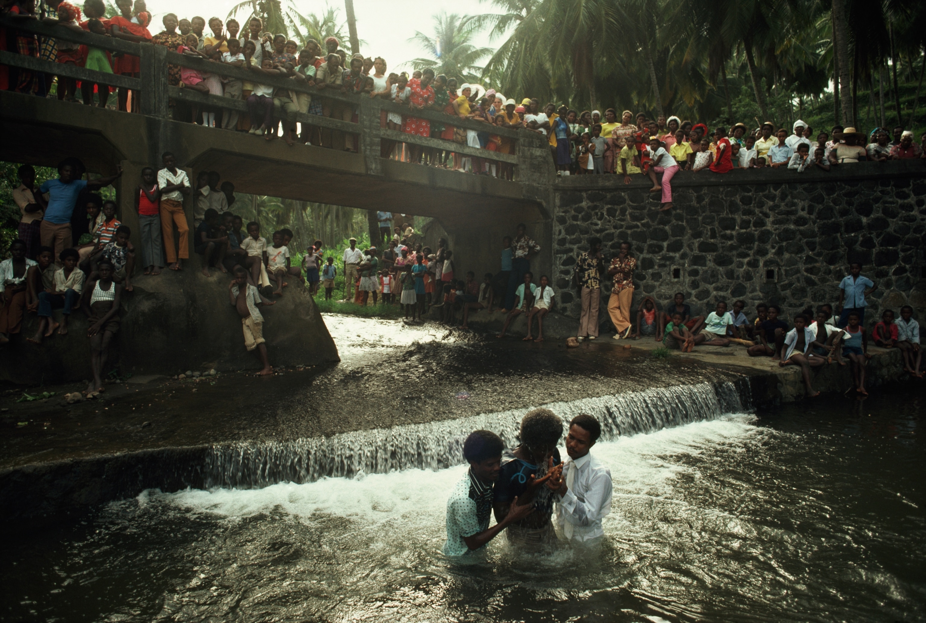 Picture of a person being baptized in a river on the island of Saint Vincent while dozens of others look on