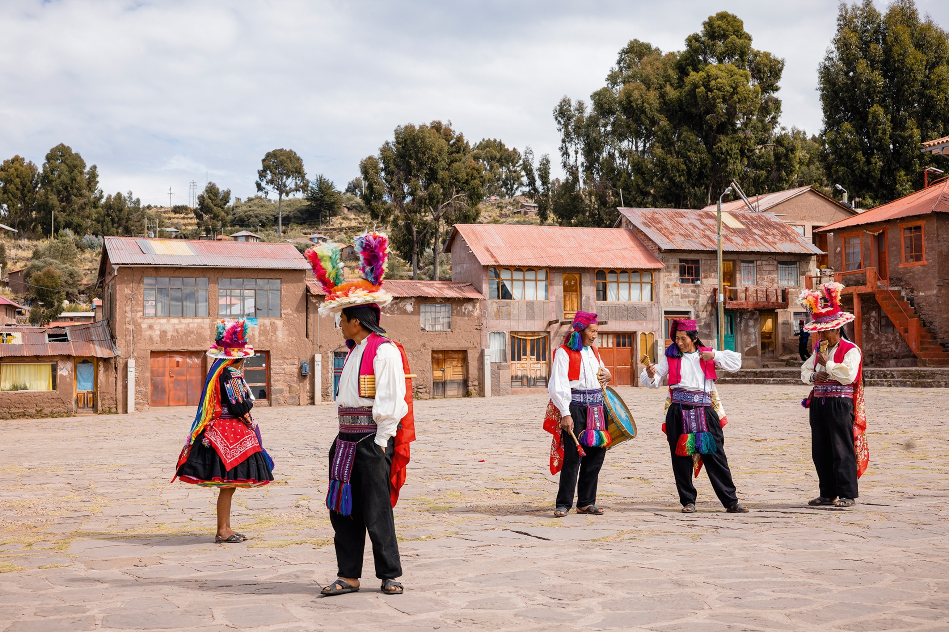A simple town square with a group of locals in traditional, colourful dress performing a dance.