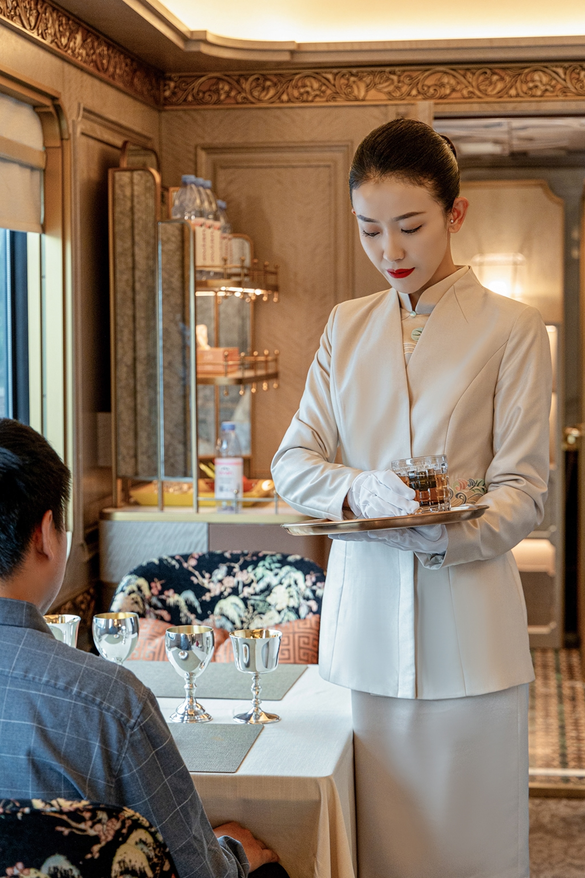 A woman in sleek waitress attire serving a drink to a customer in a train restaurant.
