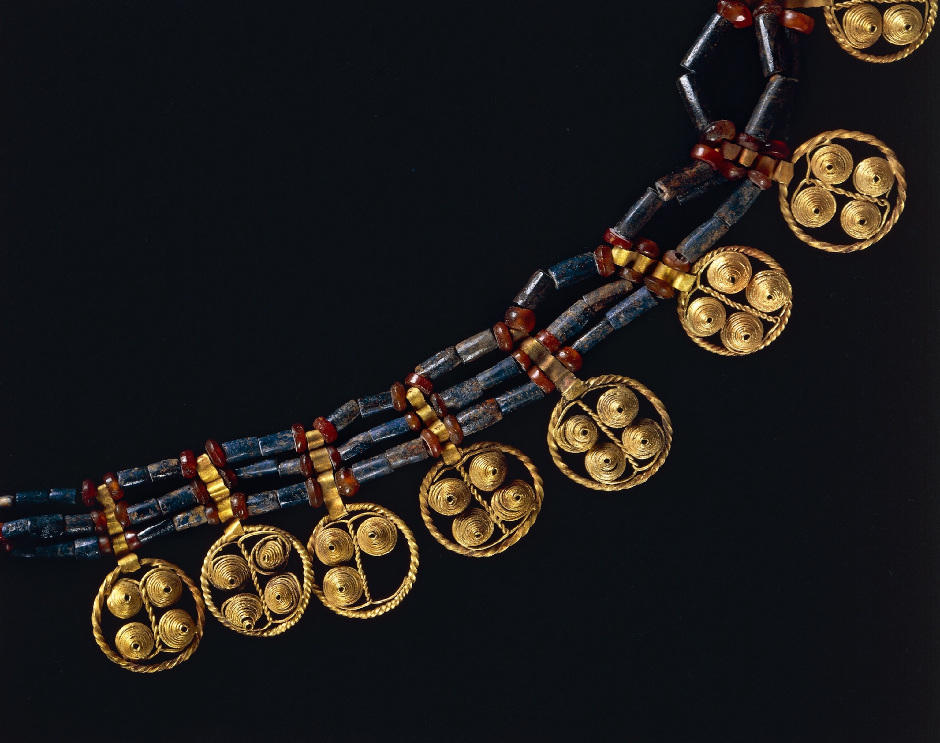 Ancient gold necklace with patterned discs, featuring blue and red beads against a black background
