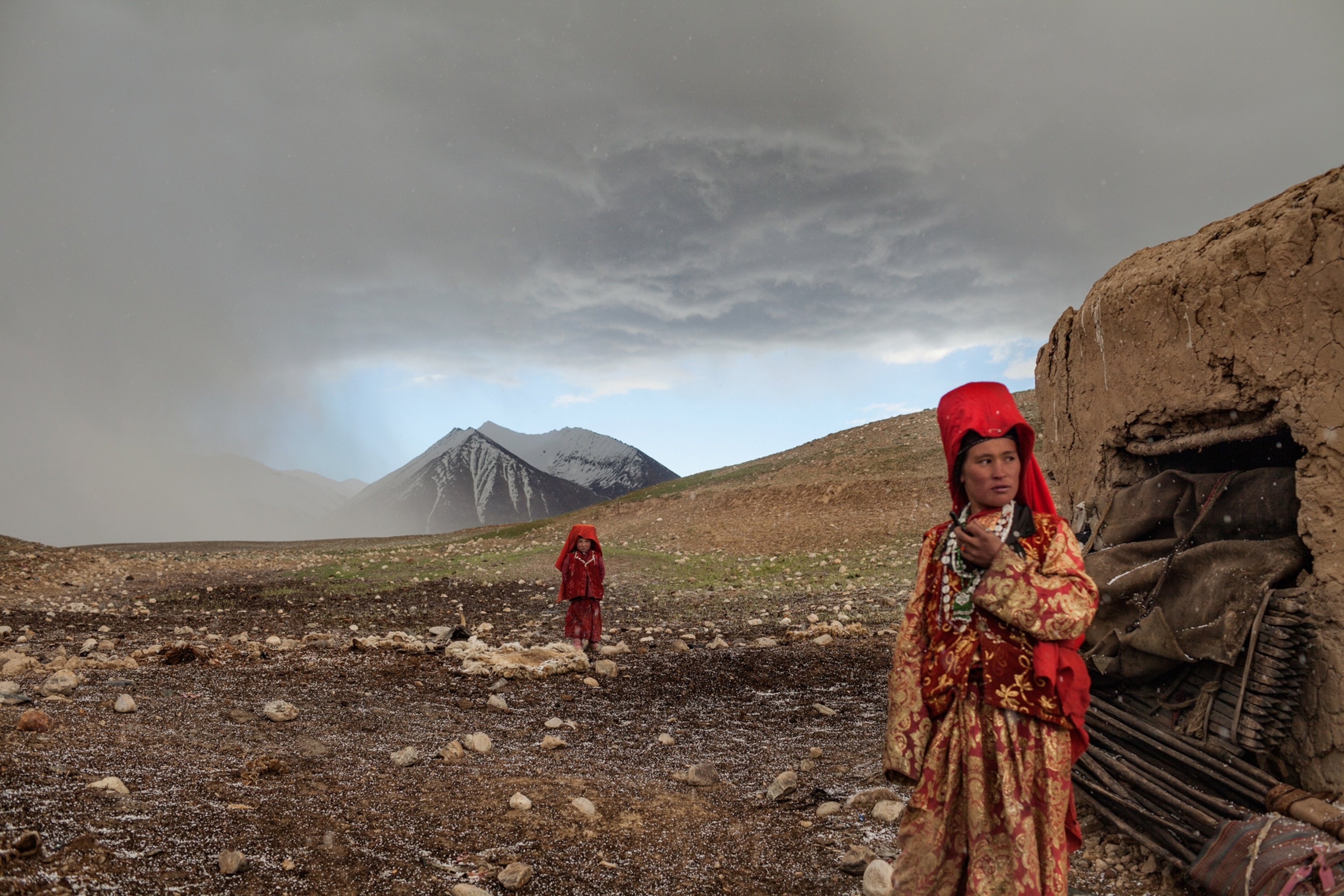 Two girls venture outside their mud hut after a hailstorm at the khan’s autumn camp beside the Aksu River. The nomads sometimes stop here for a few weeks between migratory seasons if grass for their herds is too scarce at the summer or winter camps.