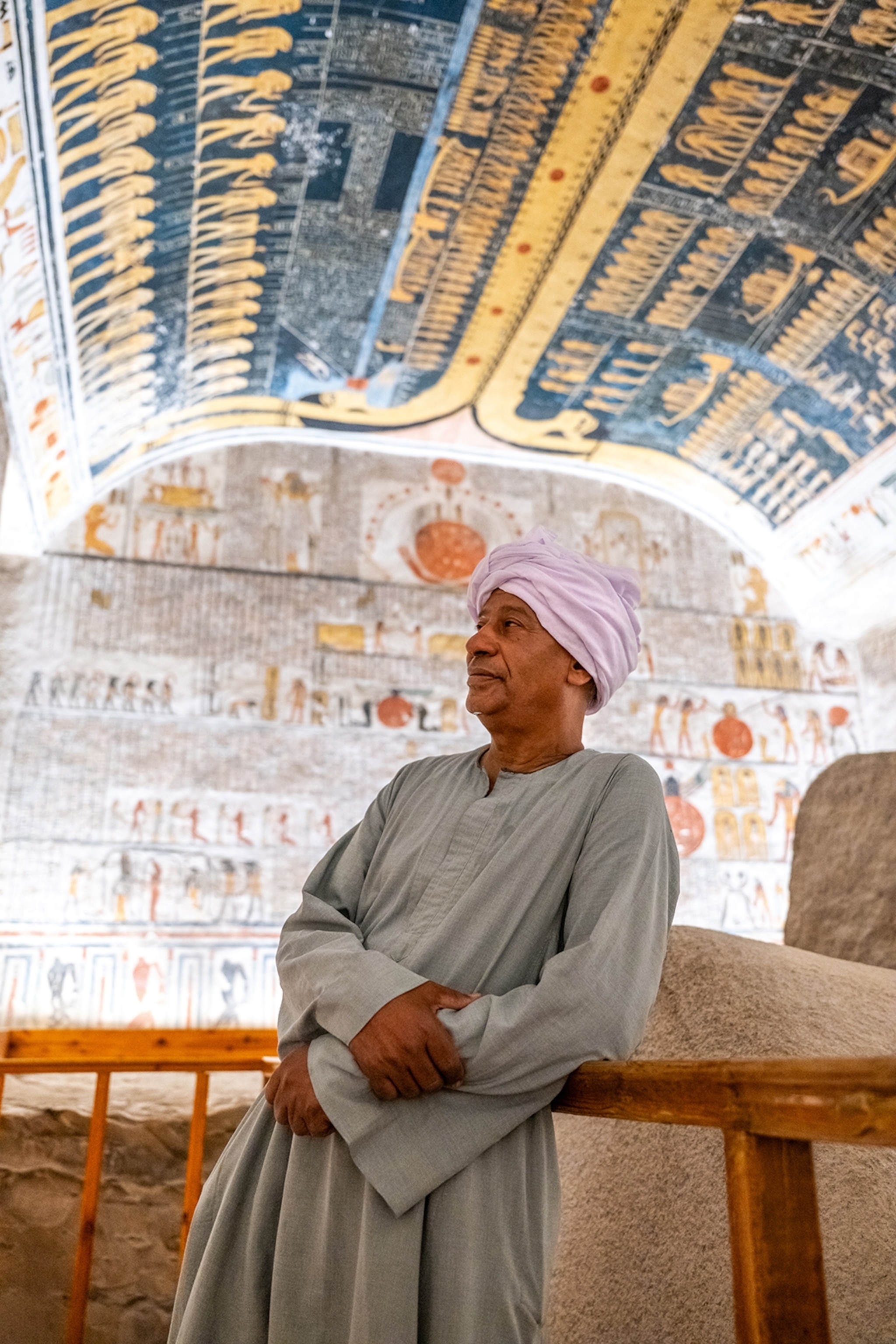 A local man wearing a tunic and turban is leaning against the railing in a richly decorated temple.