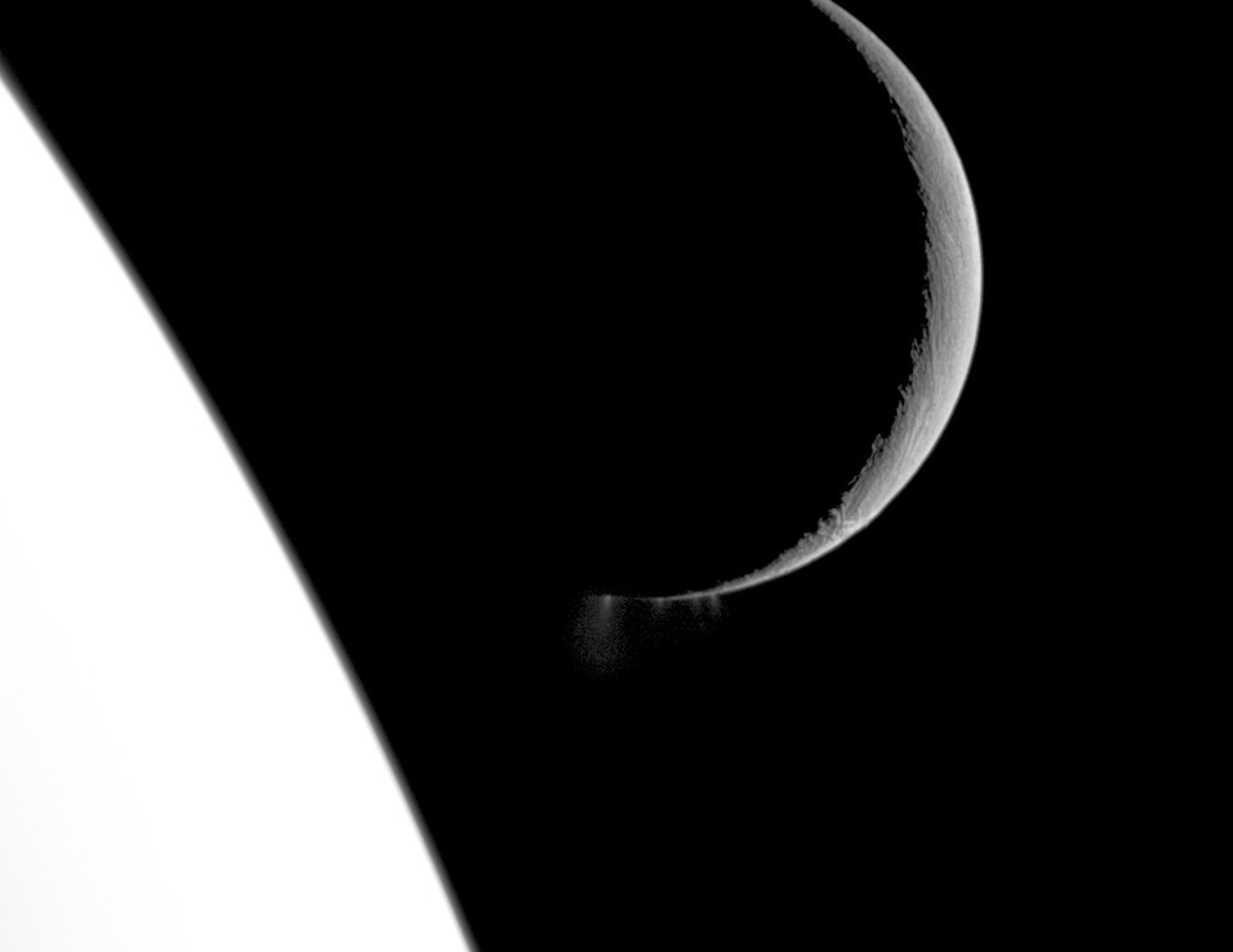 The crescent shape of the moon Enceladus is set against a bright section of its parent planet Saturn in a new picture