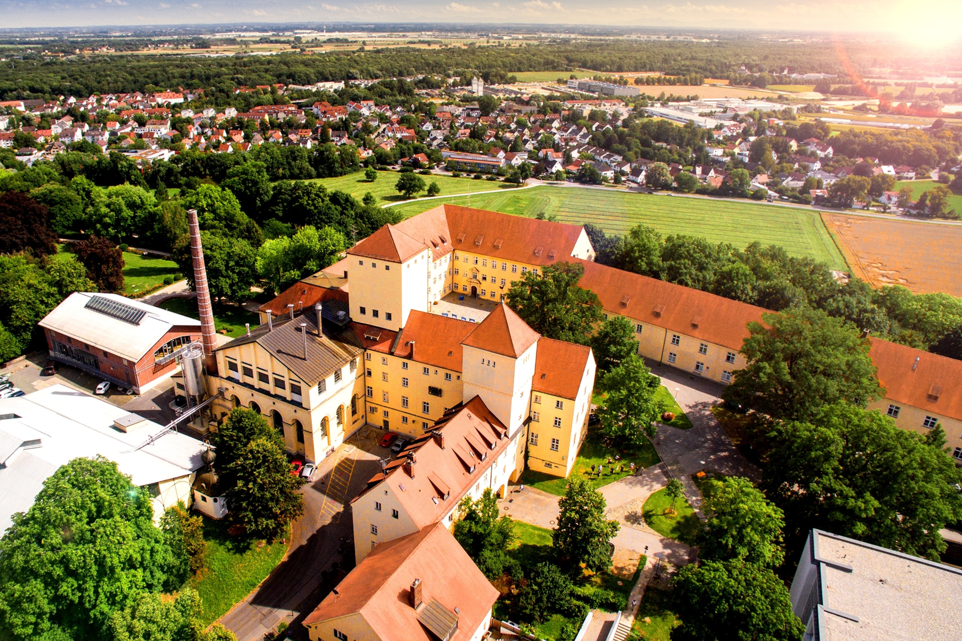 An aerial shot of a monastery-like brewery set in the midst of greenery, fields and rolling hills.