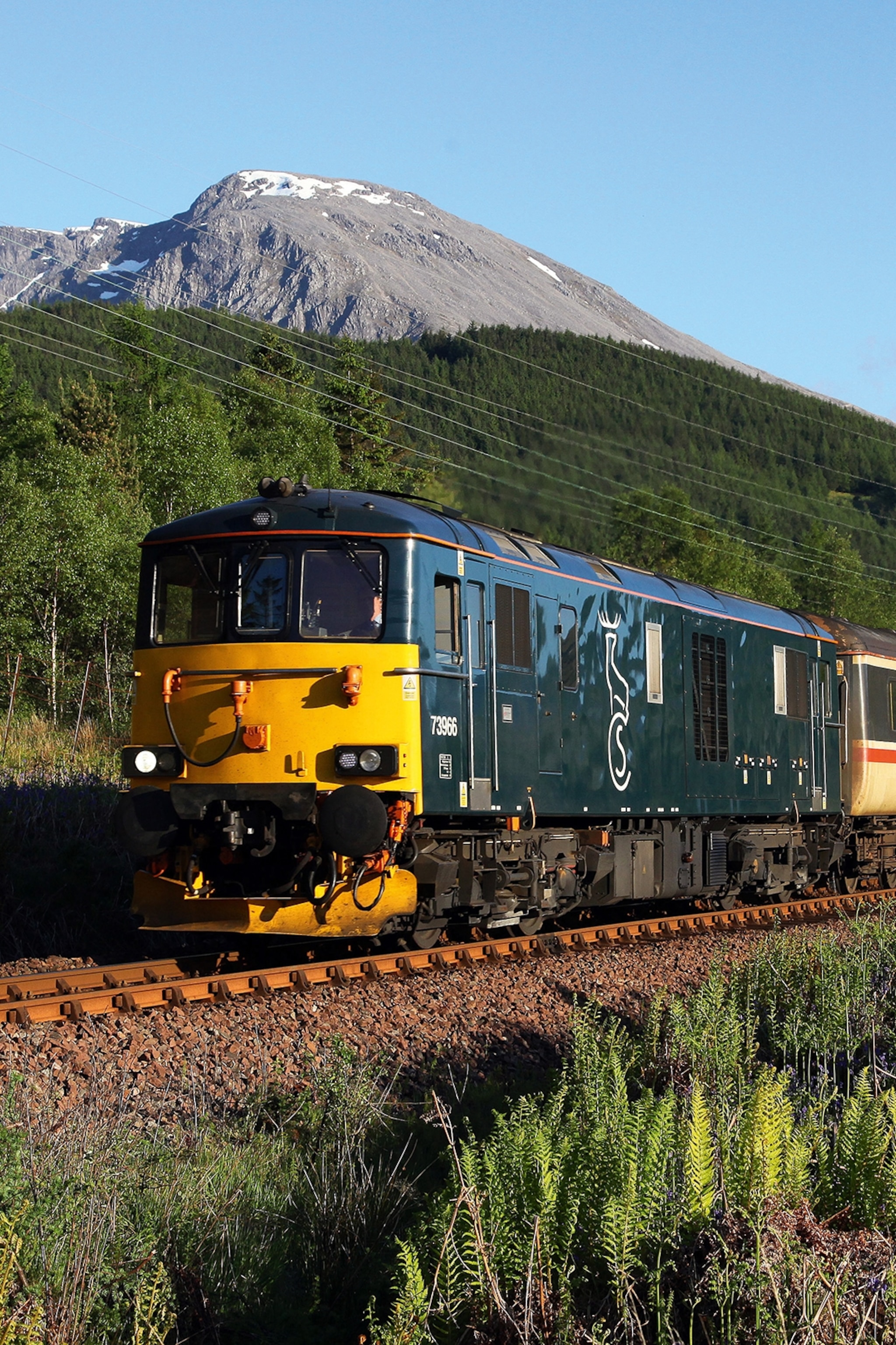 A rustic sleeper train running past snow-capped mountains.