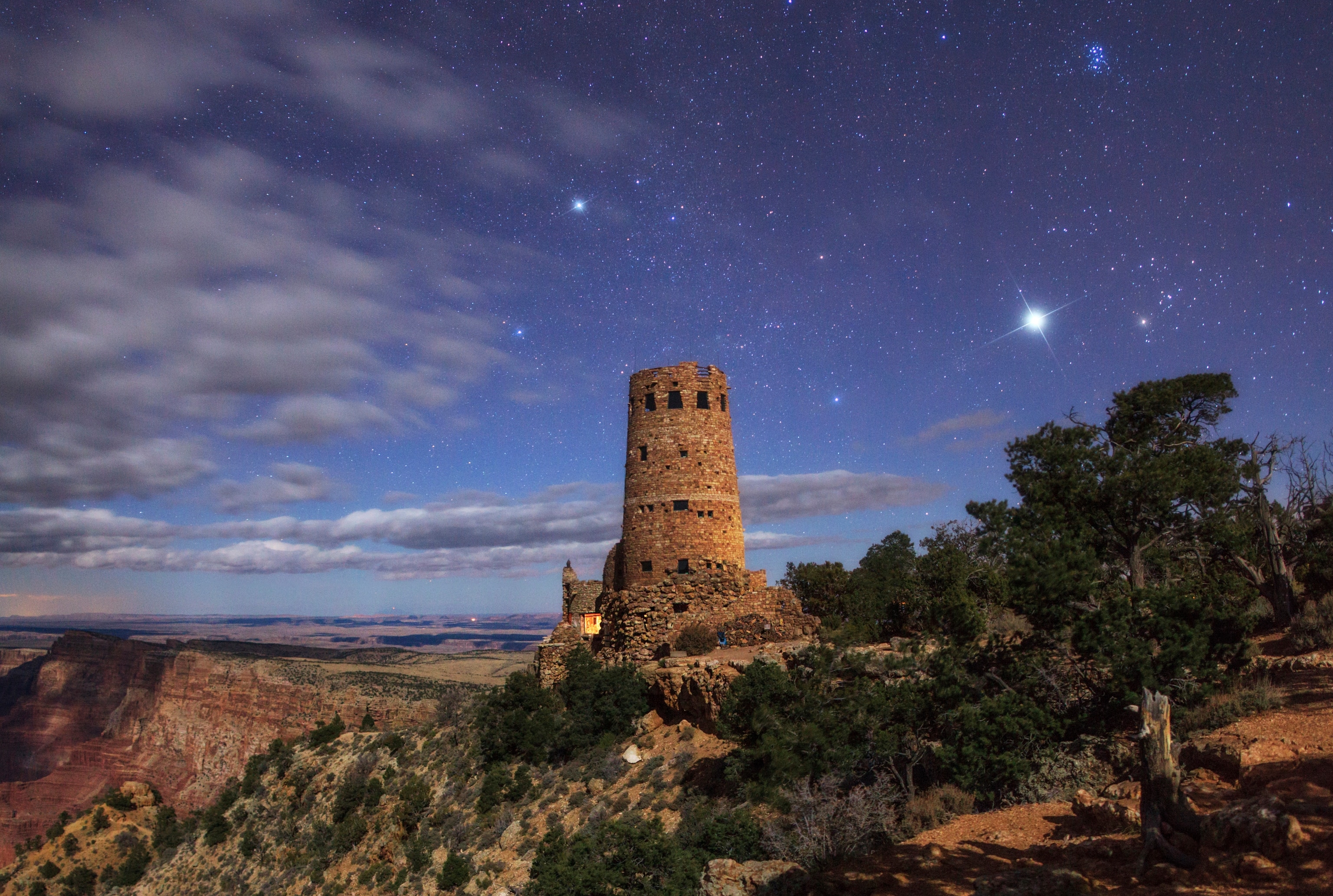 The night sky above the Grand Canyon and the Desert View Watchtower. Planet Jupiter appears in the constellation Taurus. The Pleiades star cluster is to the upper right of Jupiter. The bright star Capella, in Auriga, is above the tower.