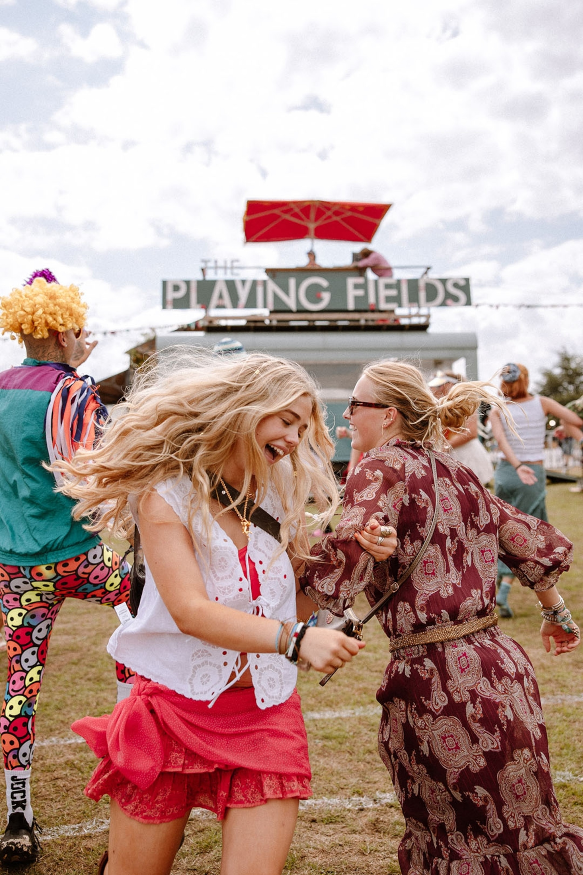 Two young women dancing on a festival field with a stage in the background.