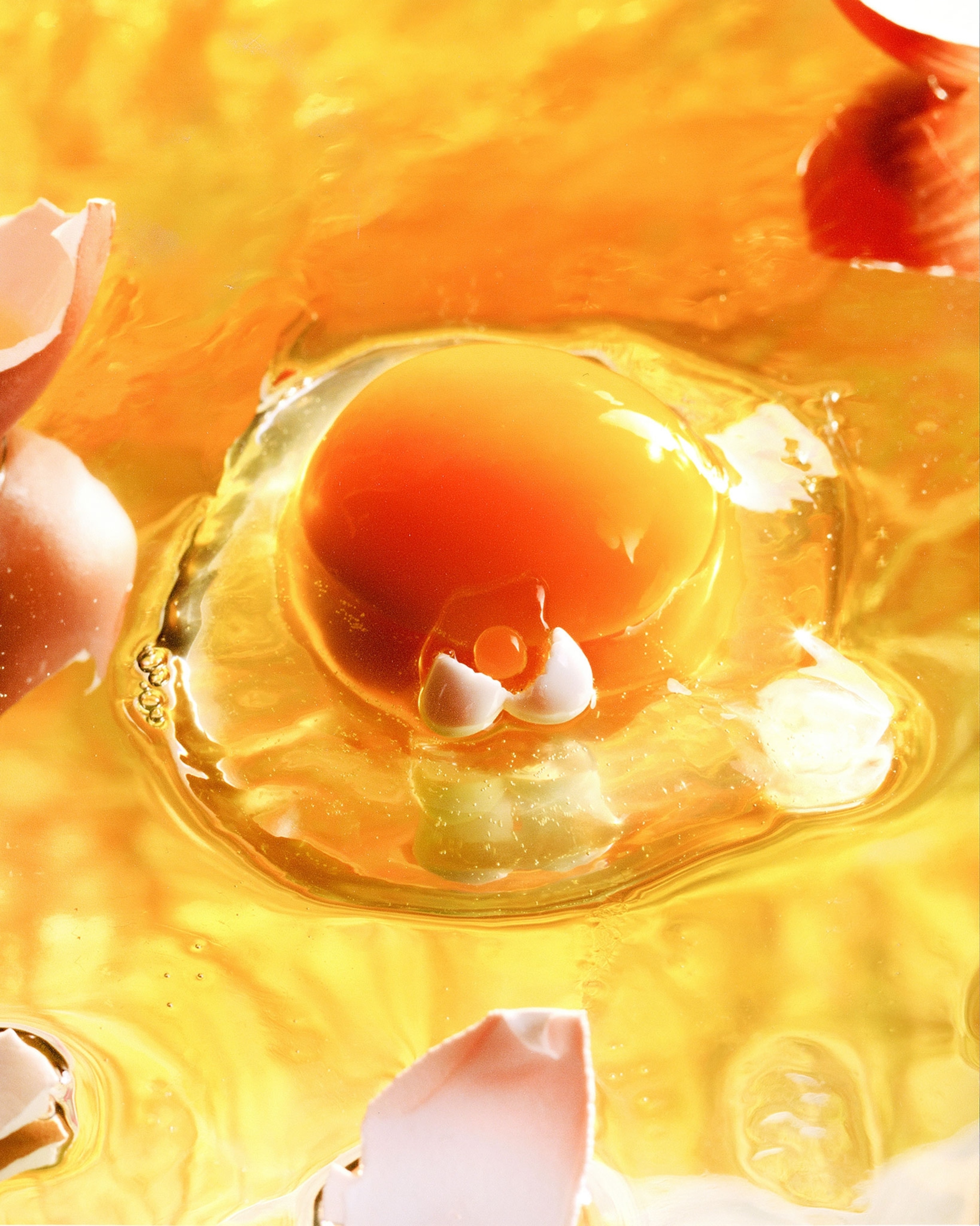 Close-up of a cracked egg with a bright orange yolk and eggshell pieces on a yellow background.