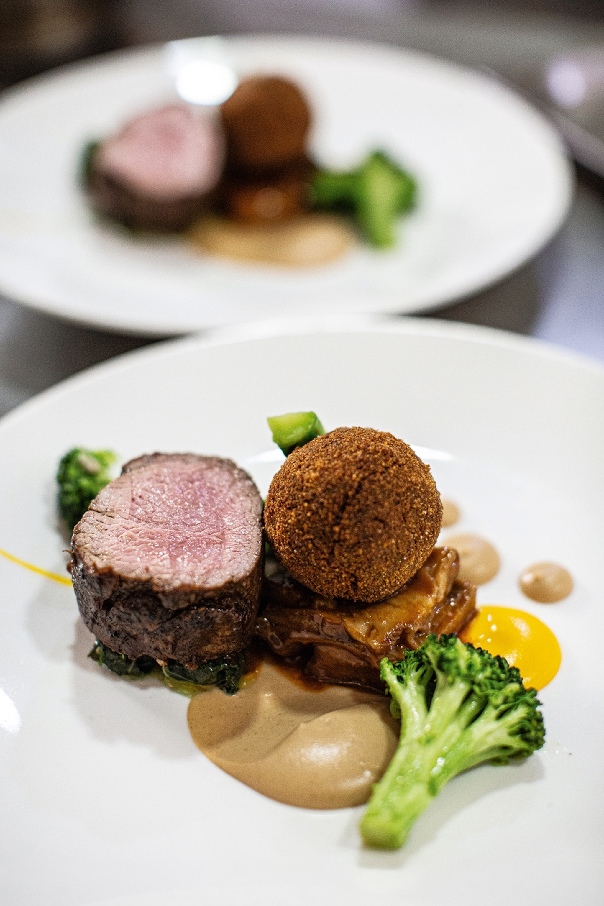 A close-up of a plat of beef steak with spiced sauces and greens.