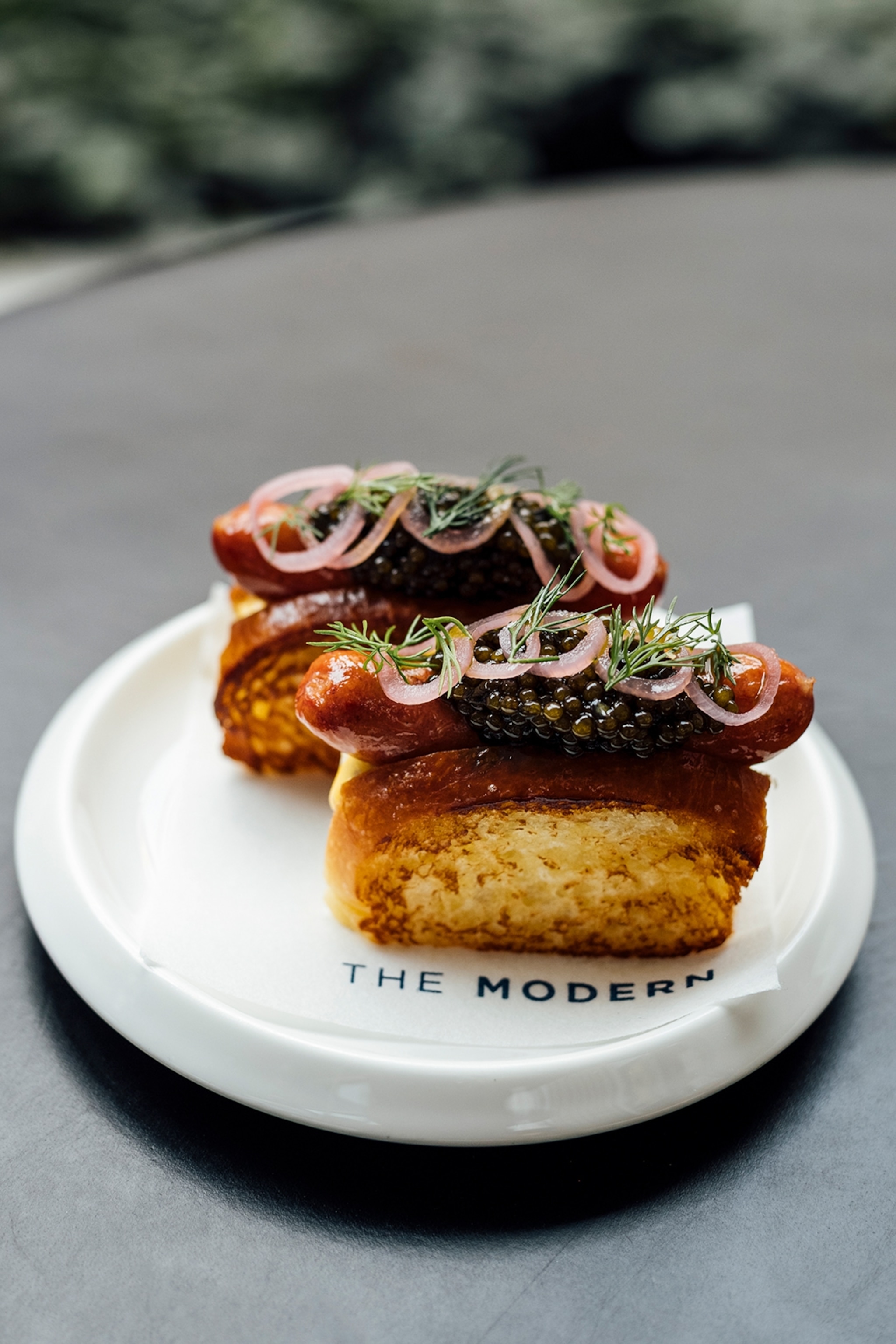 Two small hot dogs in a brioche bun topped with caviar on a white plate.