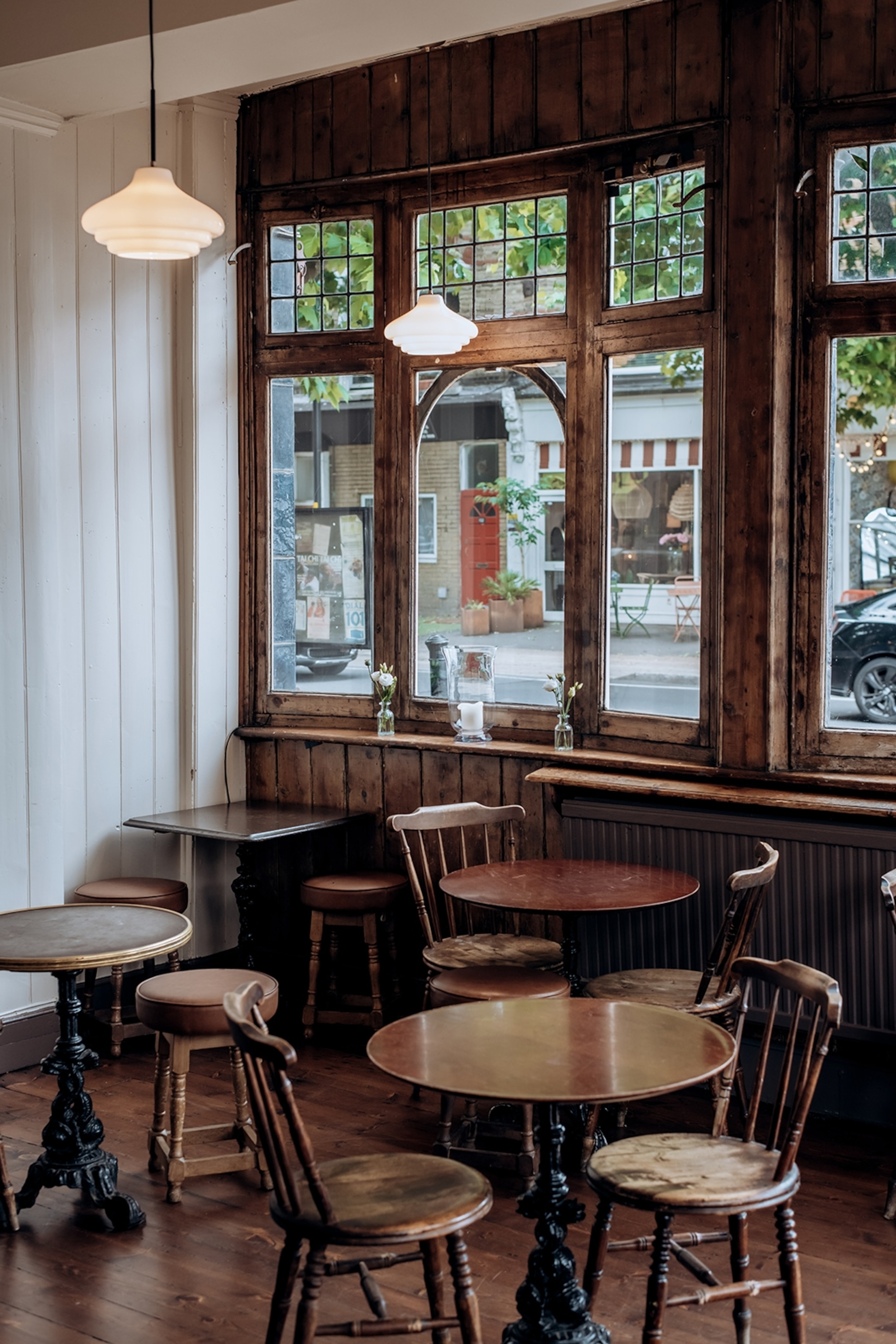 Simple wooden round tables and chairs arranged in a pub by its window front.