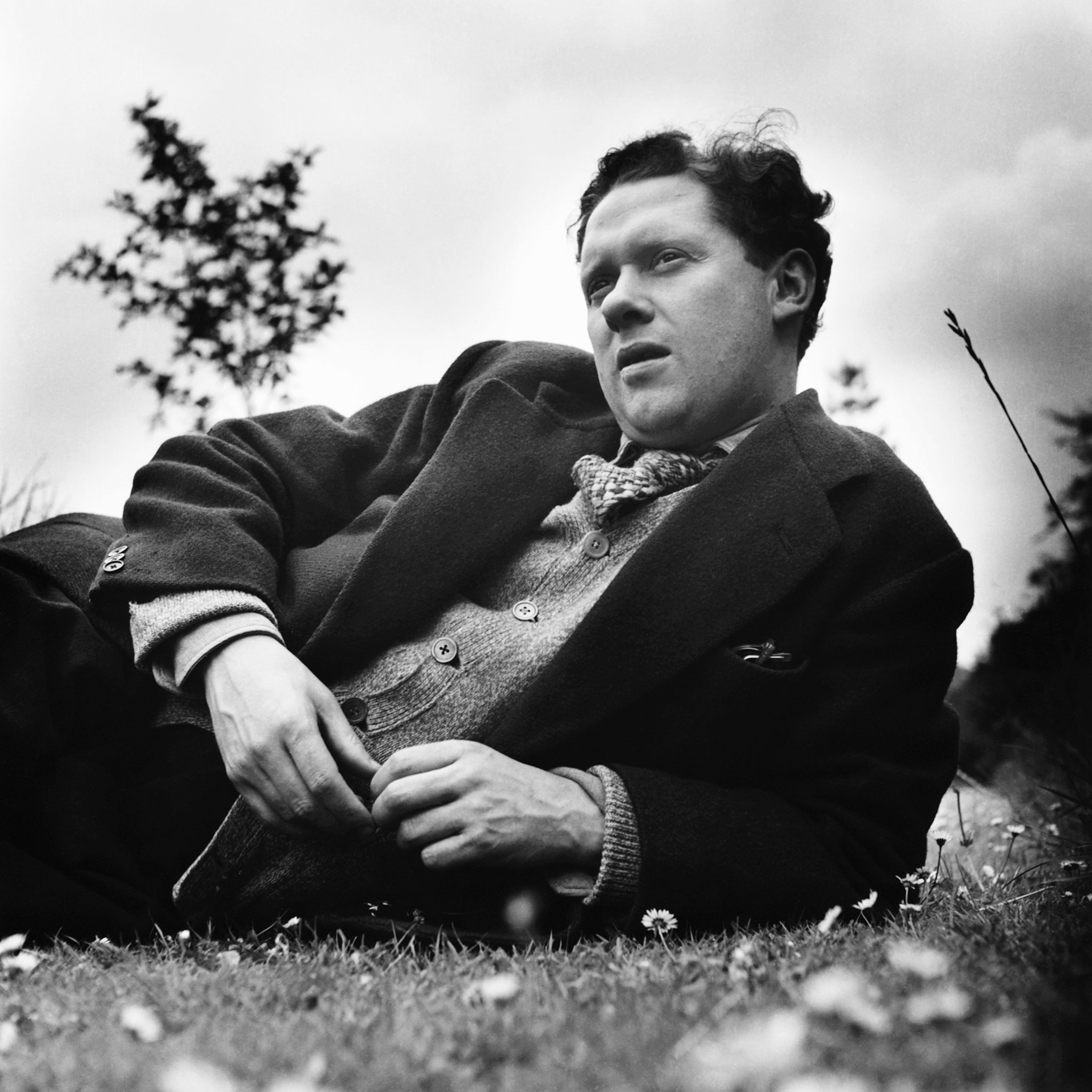 A black and white photo of a man in a suit from the 1930s, lounging in the grass with a contemplative look on his face