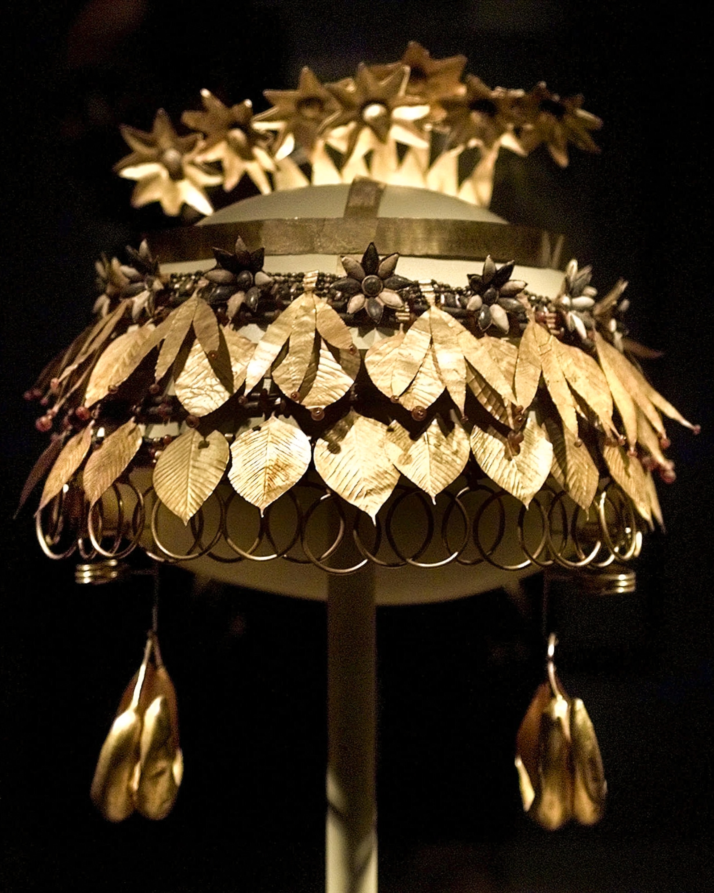 Ornate gold crown with leaf, flower motifs, and hanging elements, displayed on a stand.