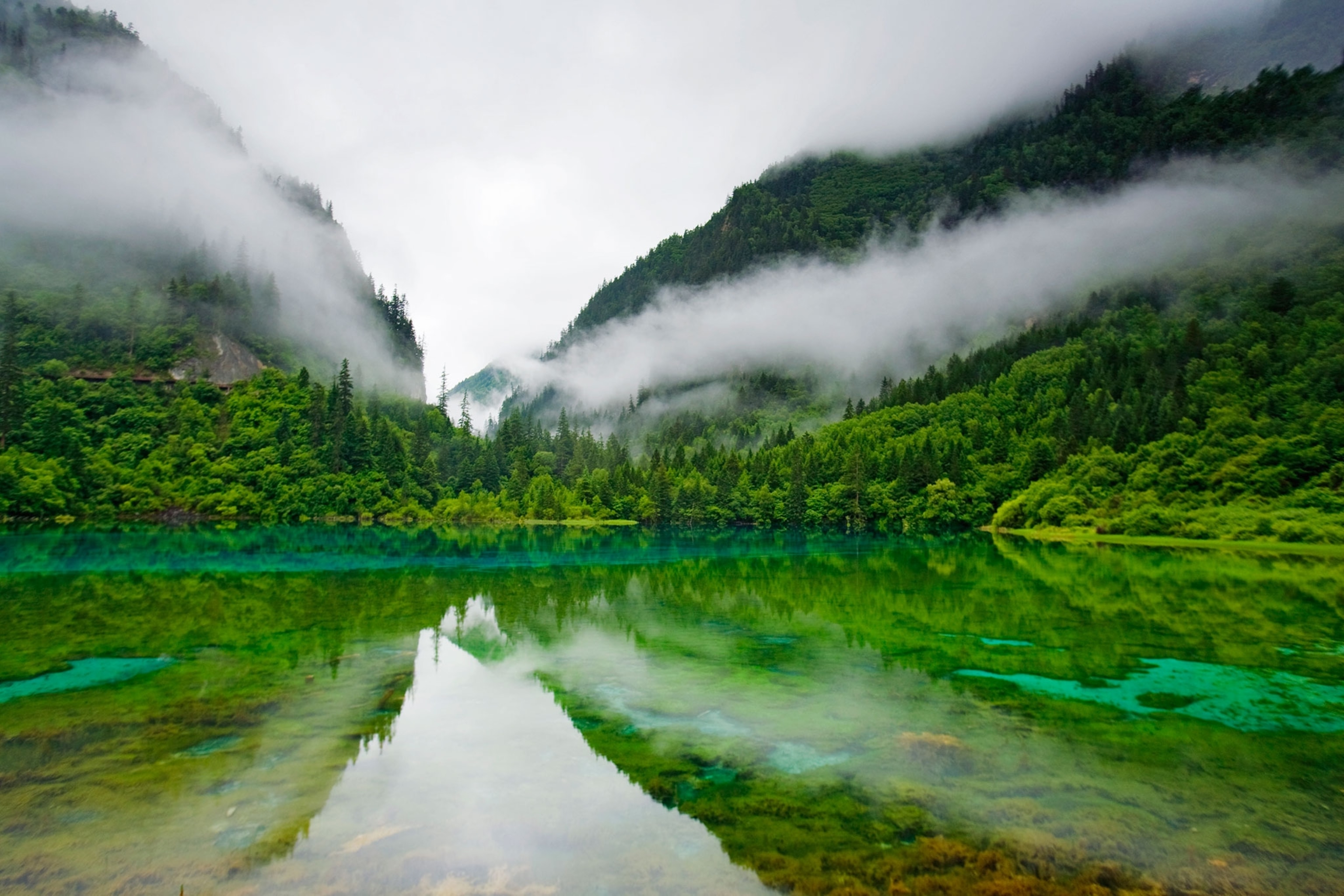 landscape image of two green mountains coming together in a valley, the scene reflected in the still water below