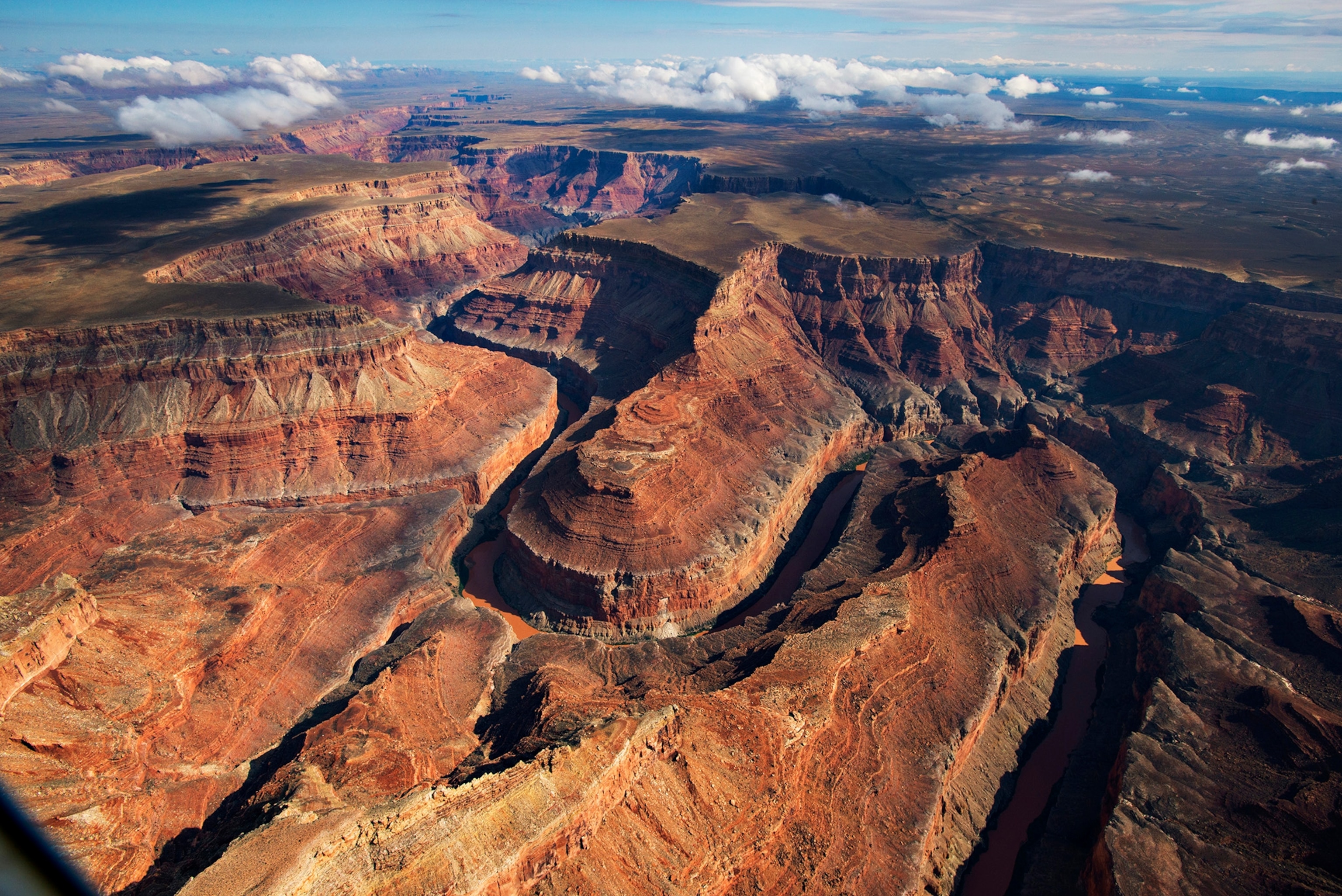 A red rock canyon cut but a river, with clouds floating in the distance