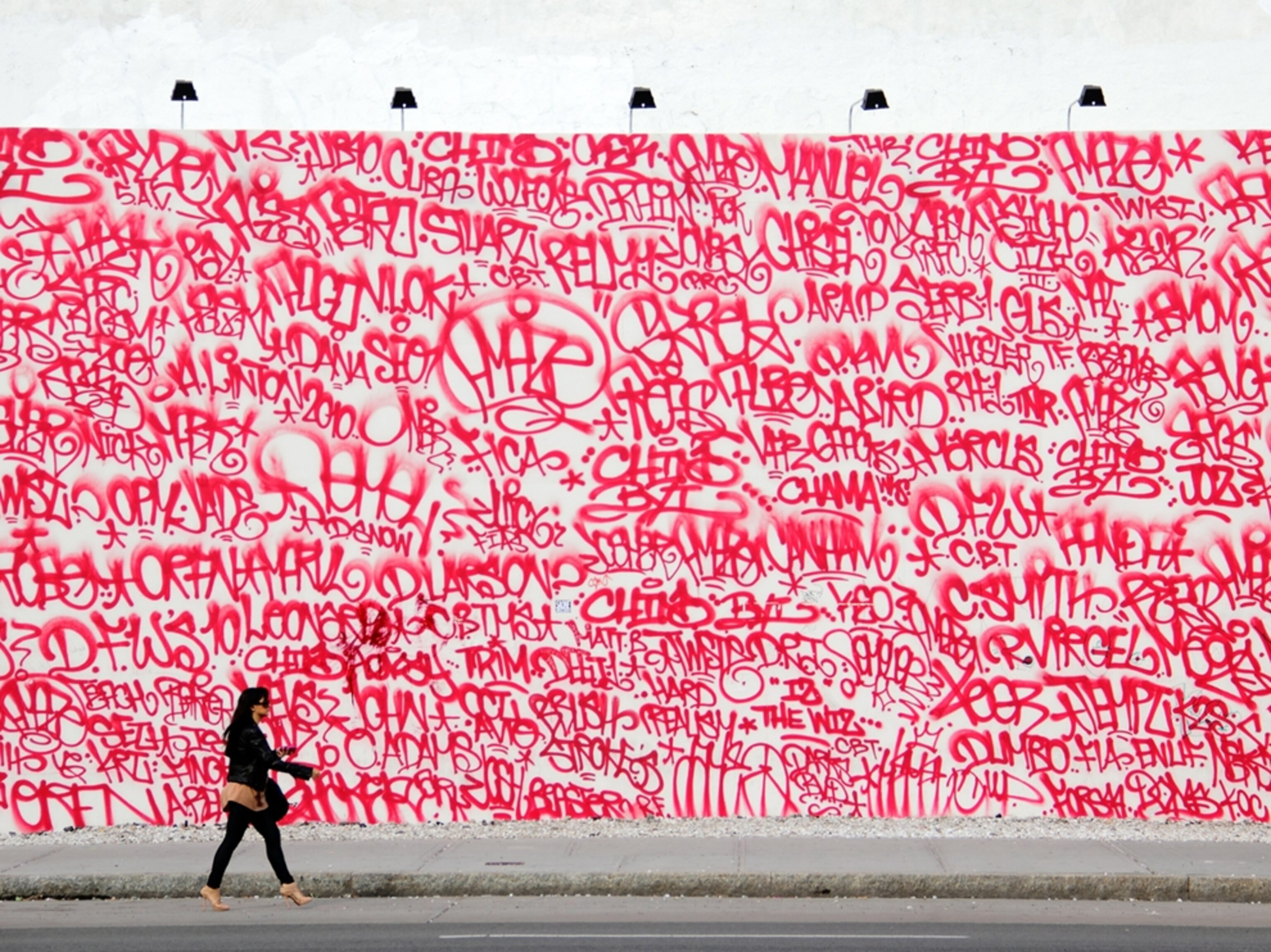 A woman walks by a wall covered in red graffiti