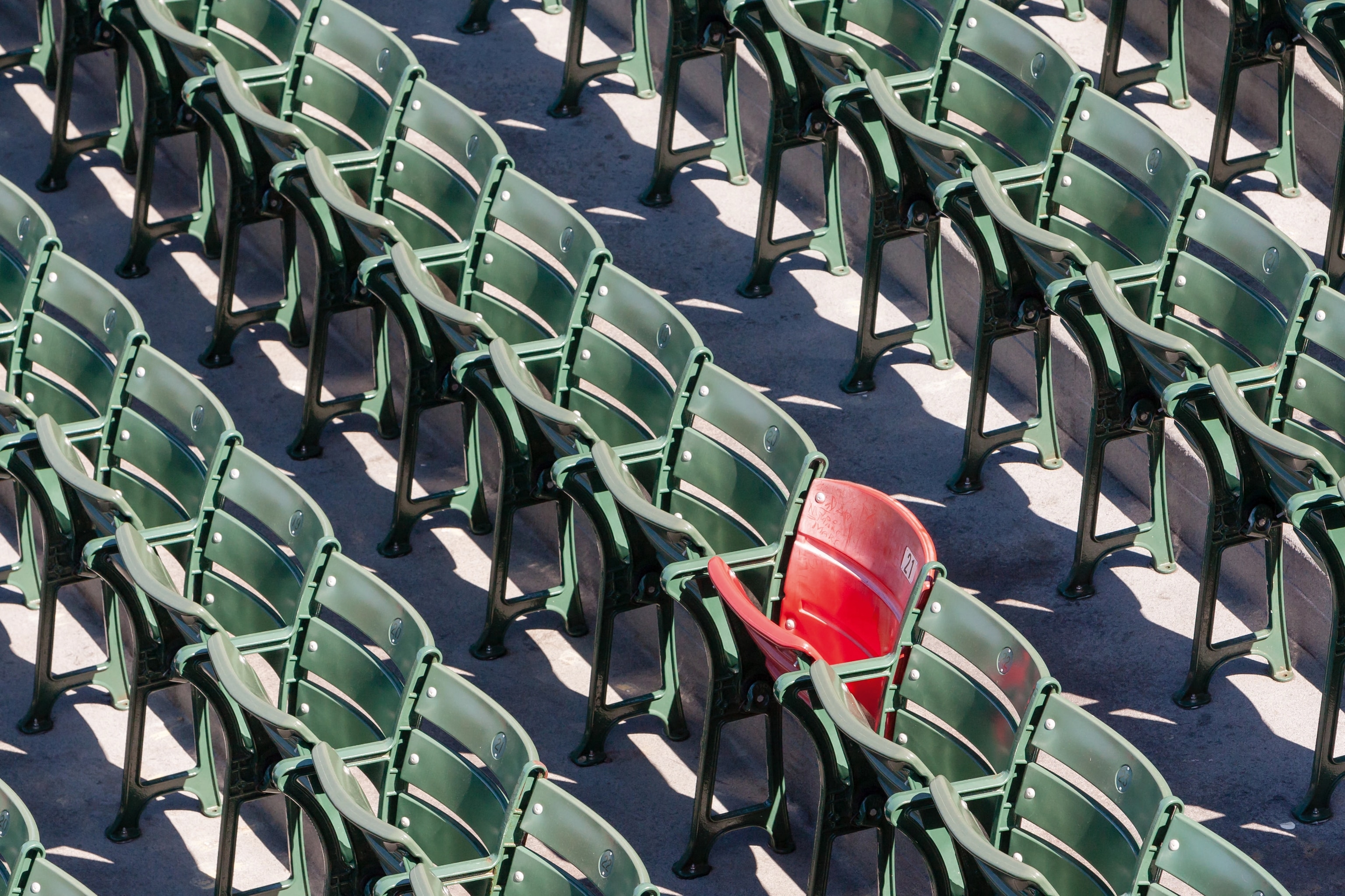 Red seat amongst other green seats in a stadium