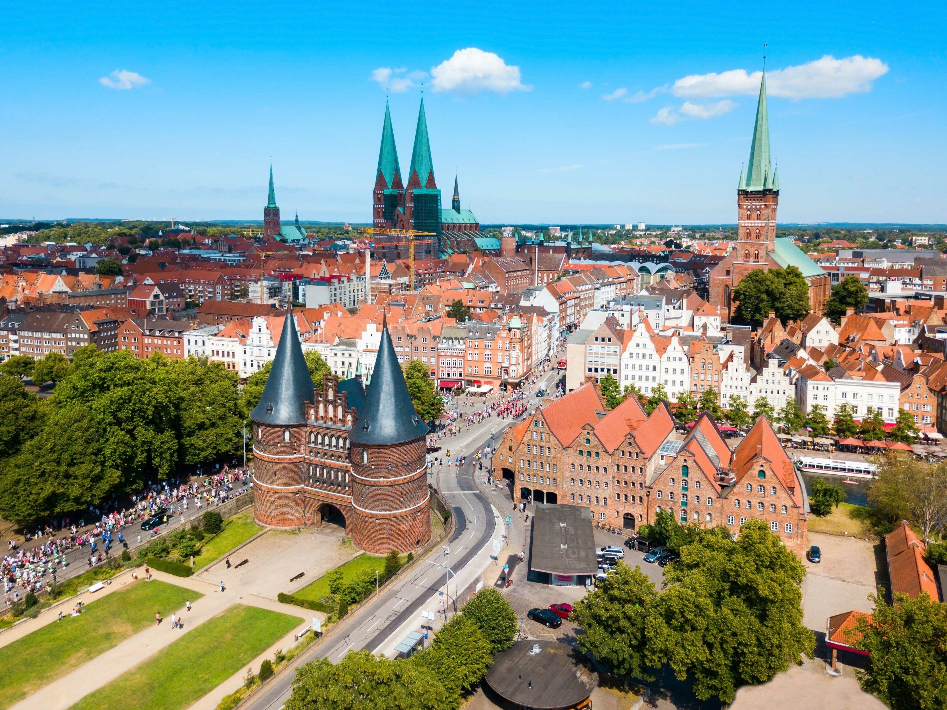 A view of Lubeck. Most of the buildings have orange roofs, except for the three large churches, which have turquoise spires.