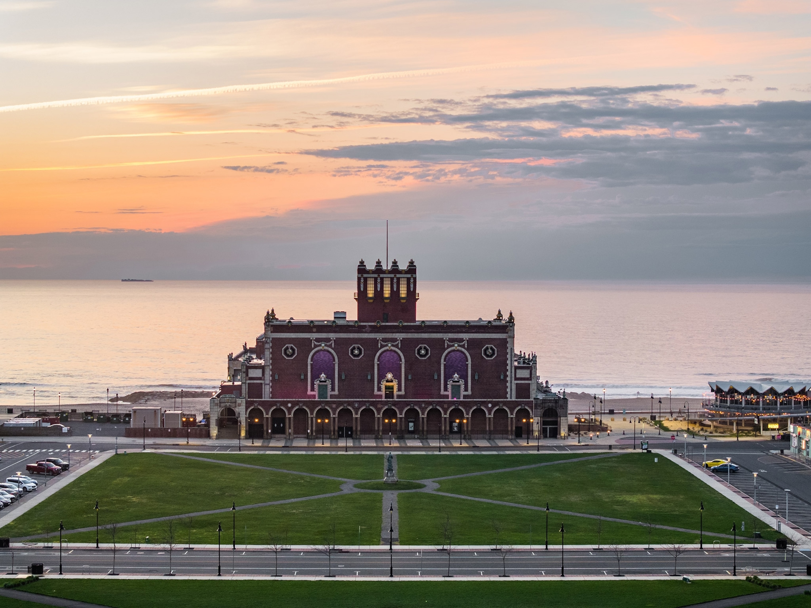 A building stands oceanfront with a tidy square in the foreground, colorful sky