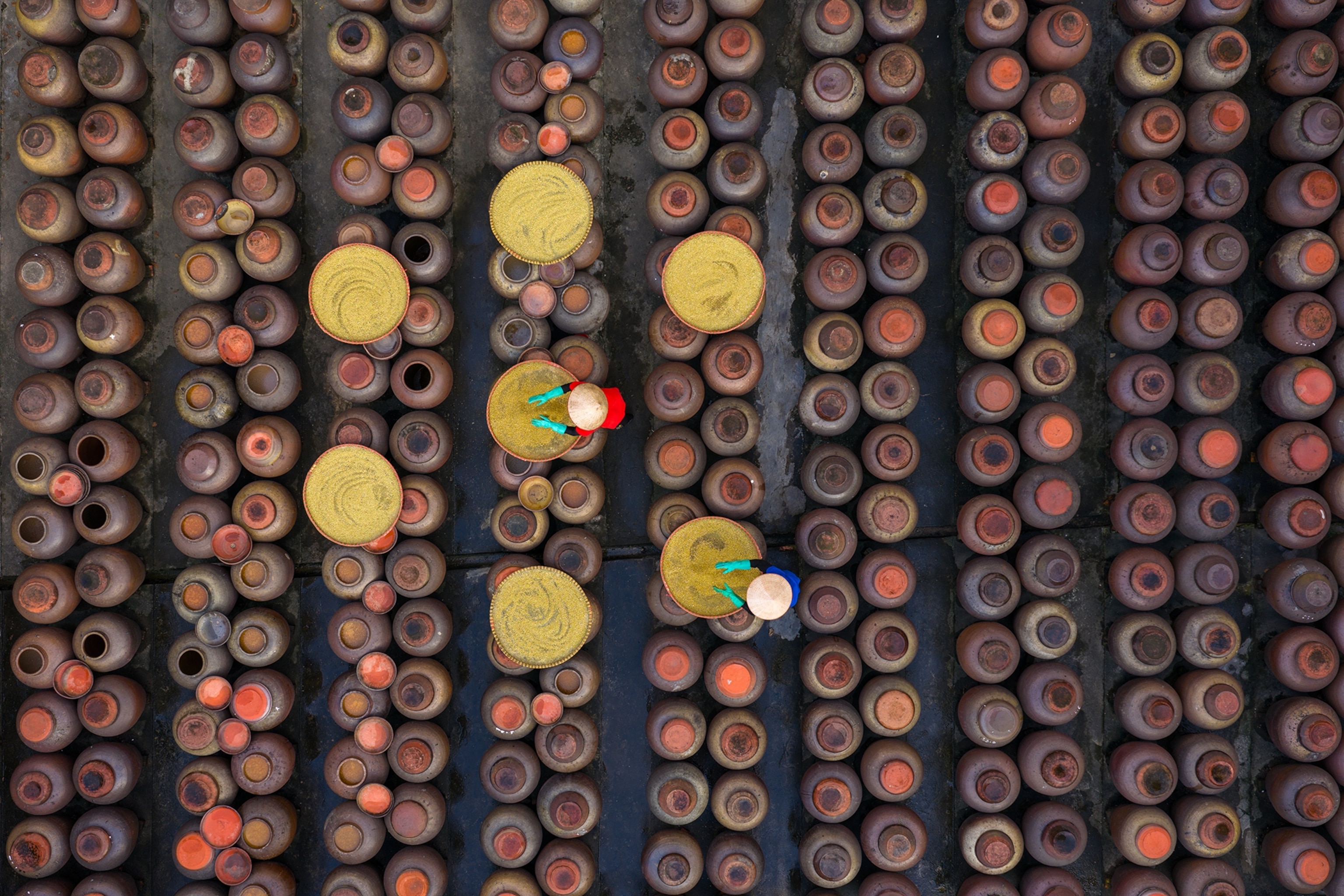 A bird's eye perspective on soy sauce pots at a factory in Hanoi with workers tending to the clay pots.